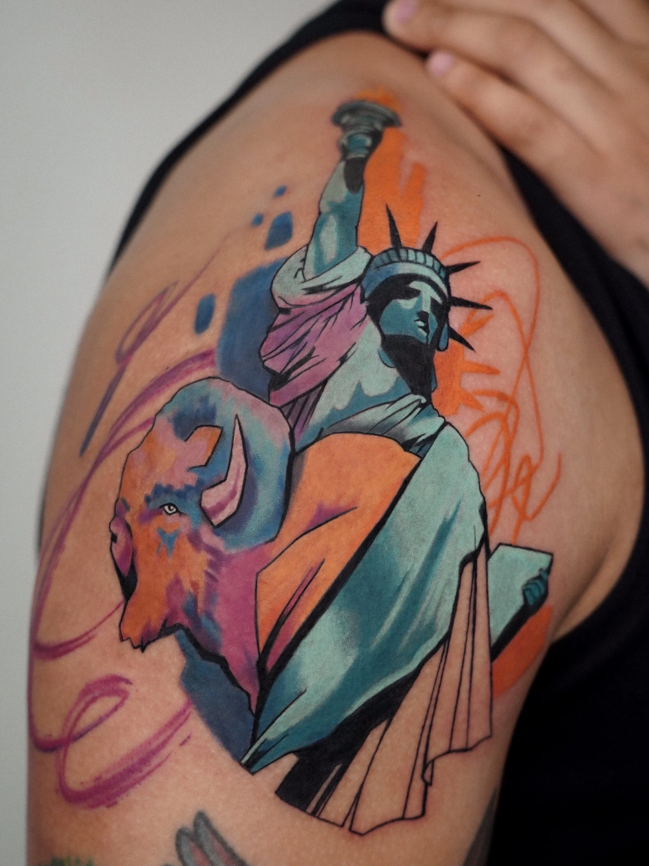 Colorful tattoo of the Statue of Liberty with a lion's head on a person's upper arm.