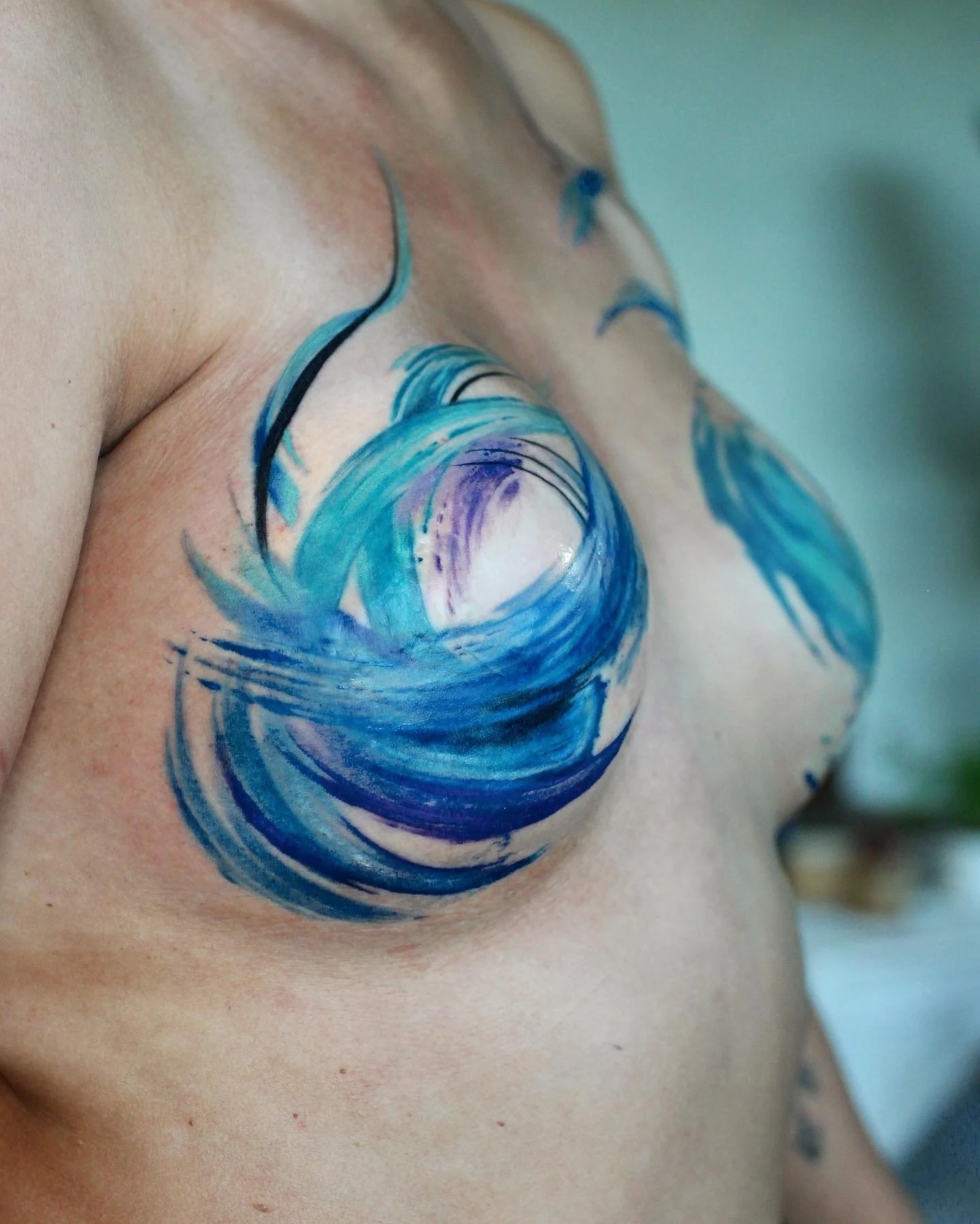 A close-up of a person's chest with a painted design resembling a blue ocean wave.