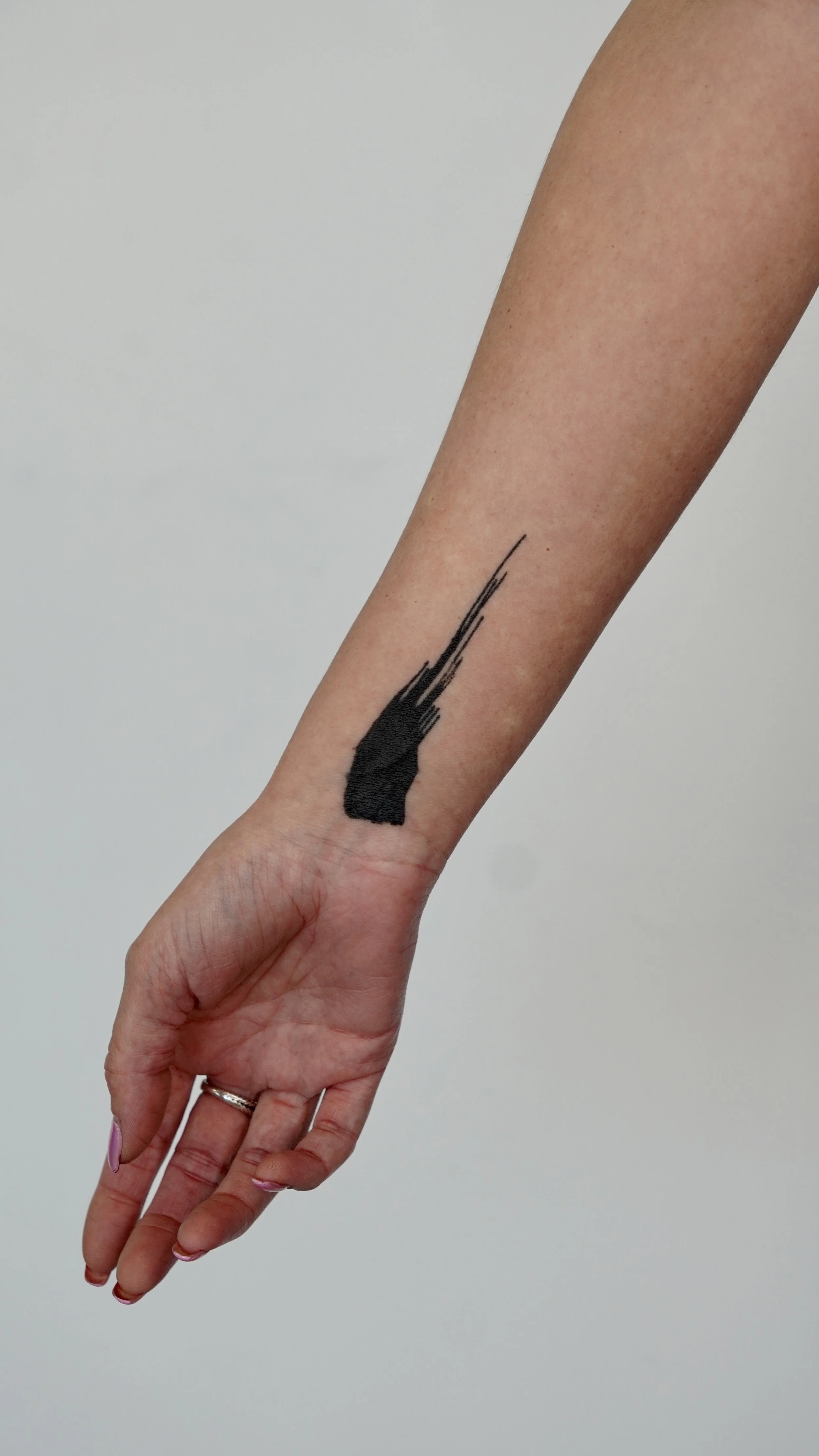 A person's arm with a black abstract tattoo extending from the wrist towards the middle of the forearm, with some parts of the tattoo appearing textured.
