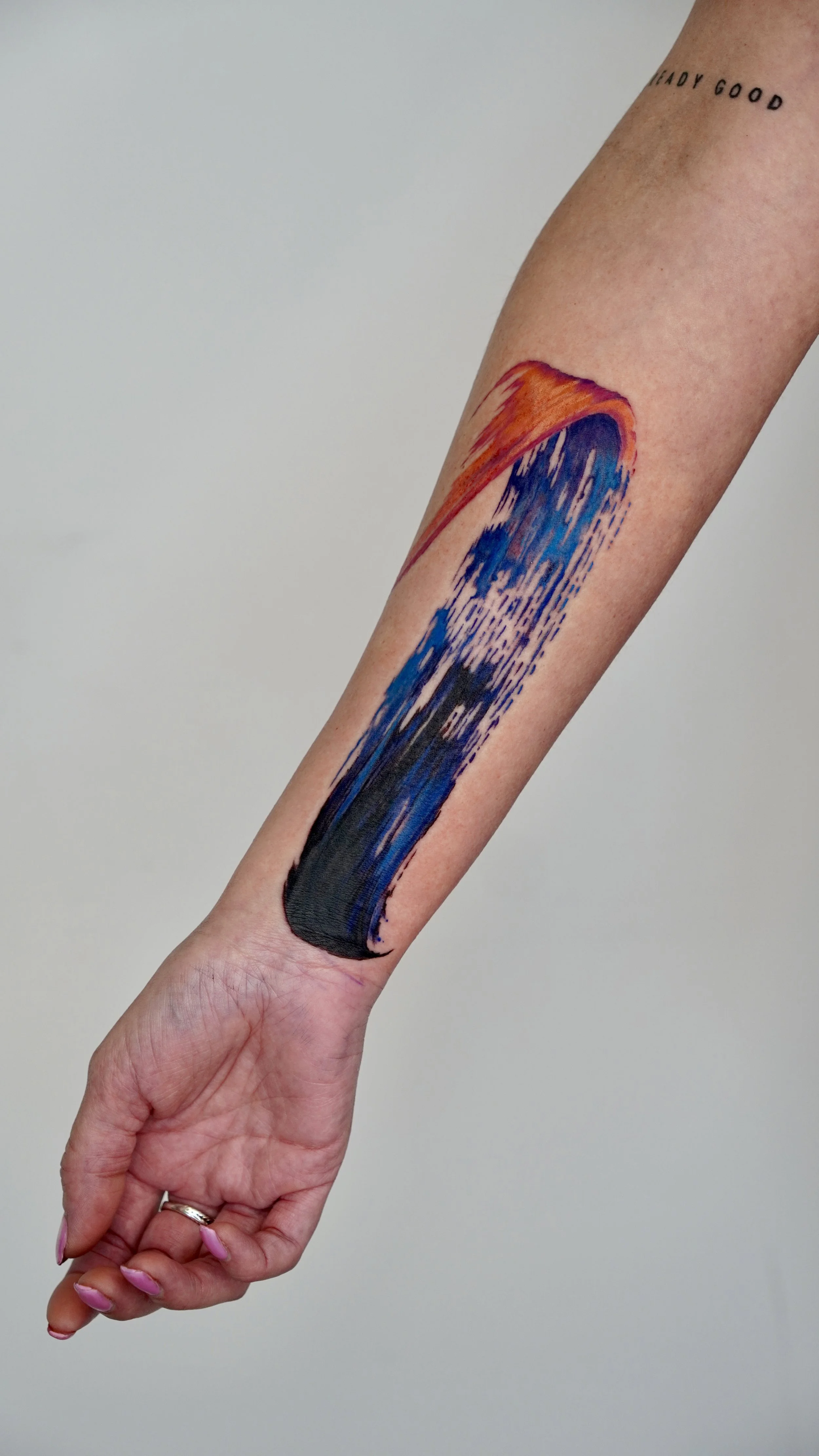 Arm with abstract tattoo featuring a flowing streak of orange, purple, blue, and black colors.