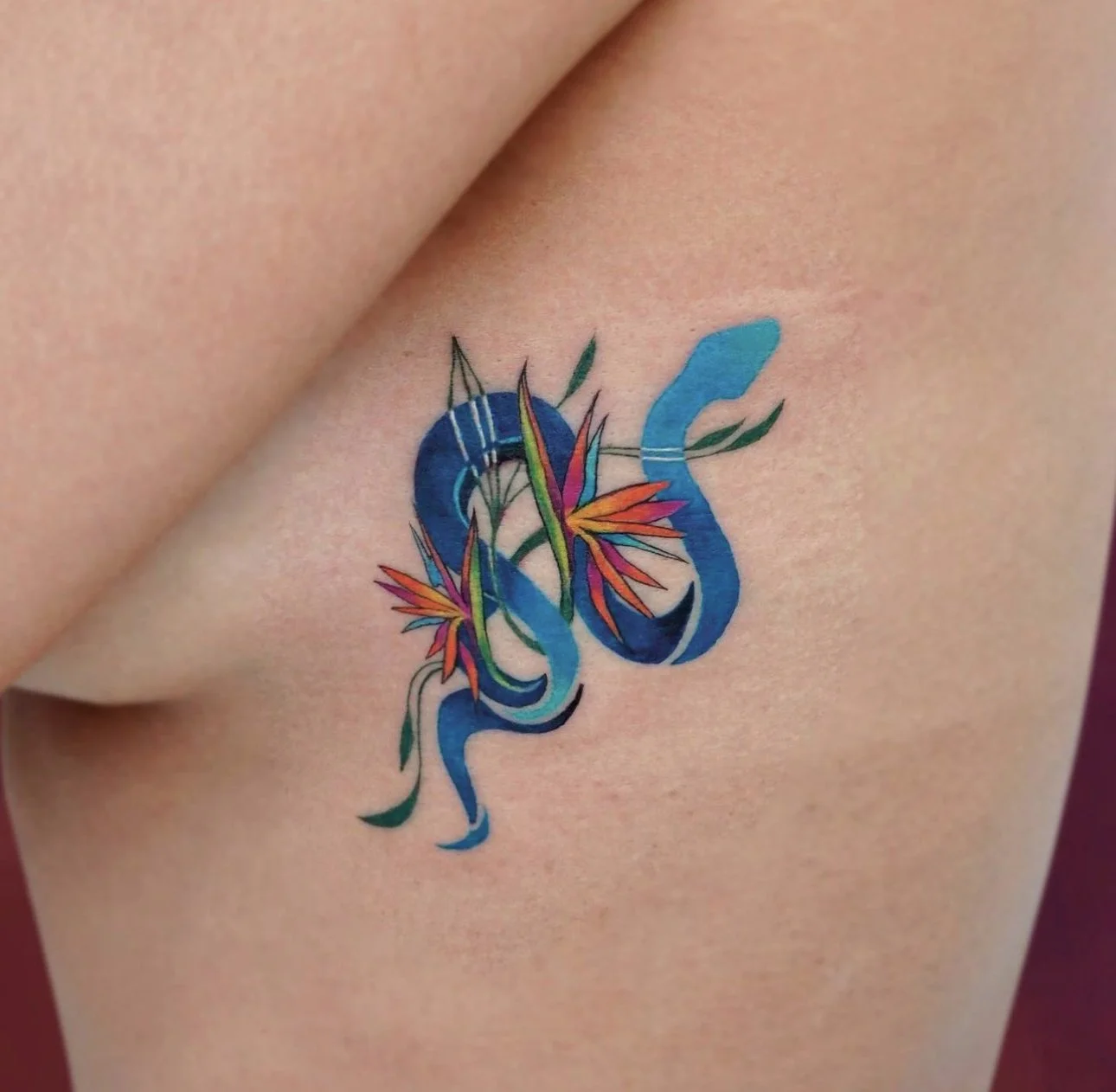 Colorful tattoo of a blue snake intertwined with orange and red flowers on skin.