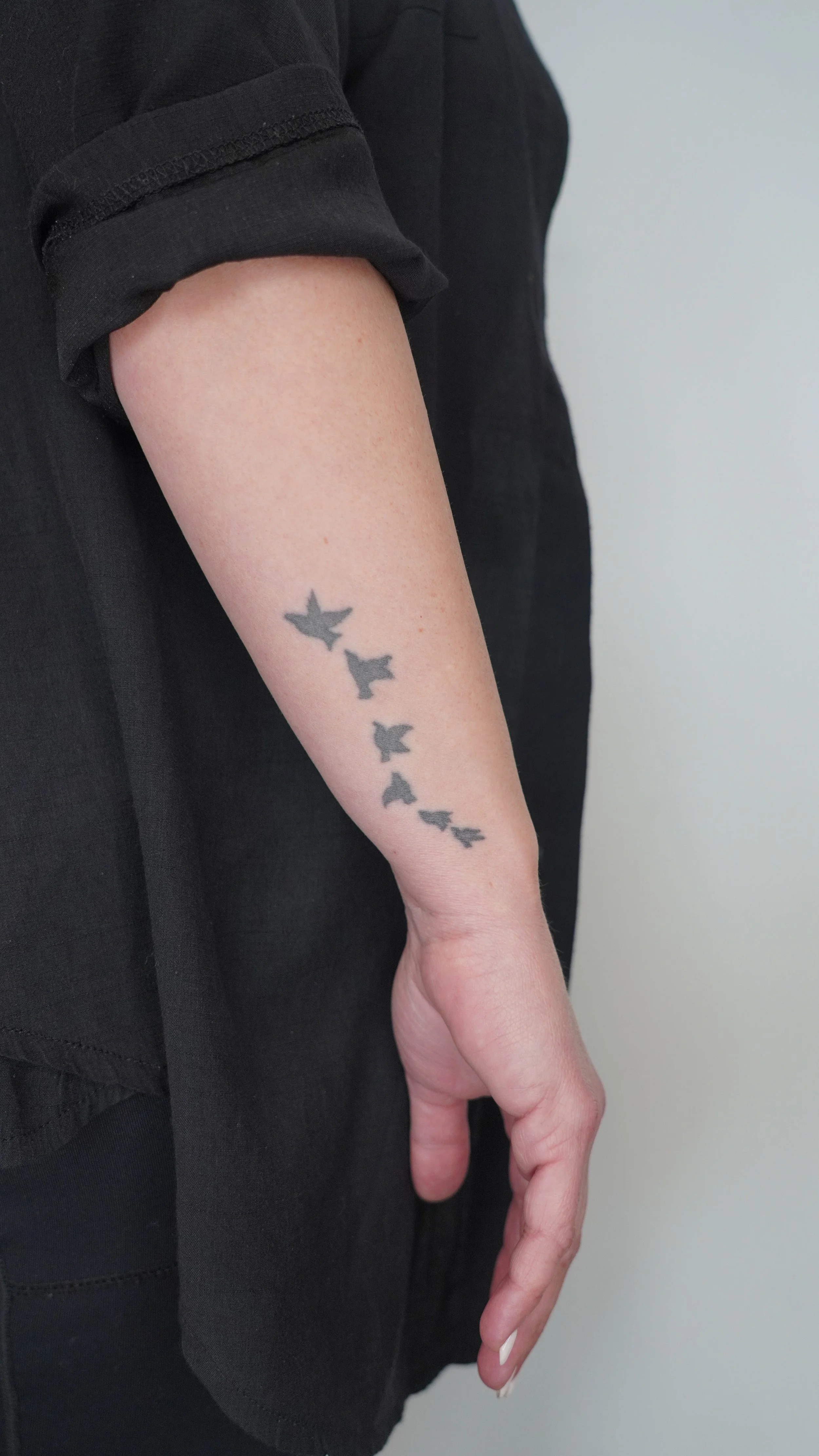 A person's arm with a tattoo of five black bird silhouettes flying downward.