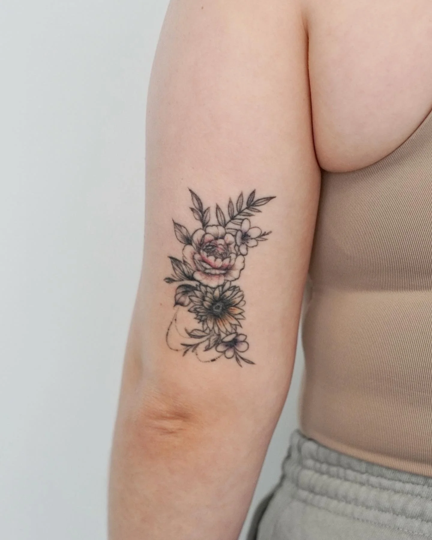 A tattoo of a floral bouquet on a person's upper arm, including a large pinkish flower, smaller flowers, and green leaves.