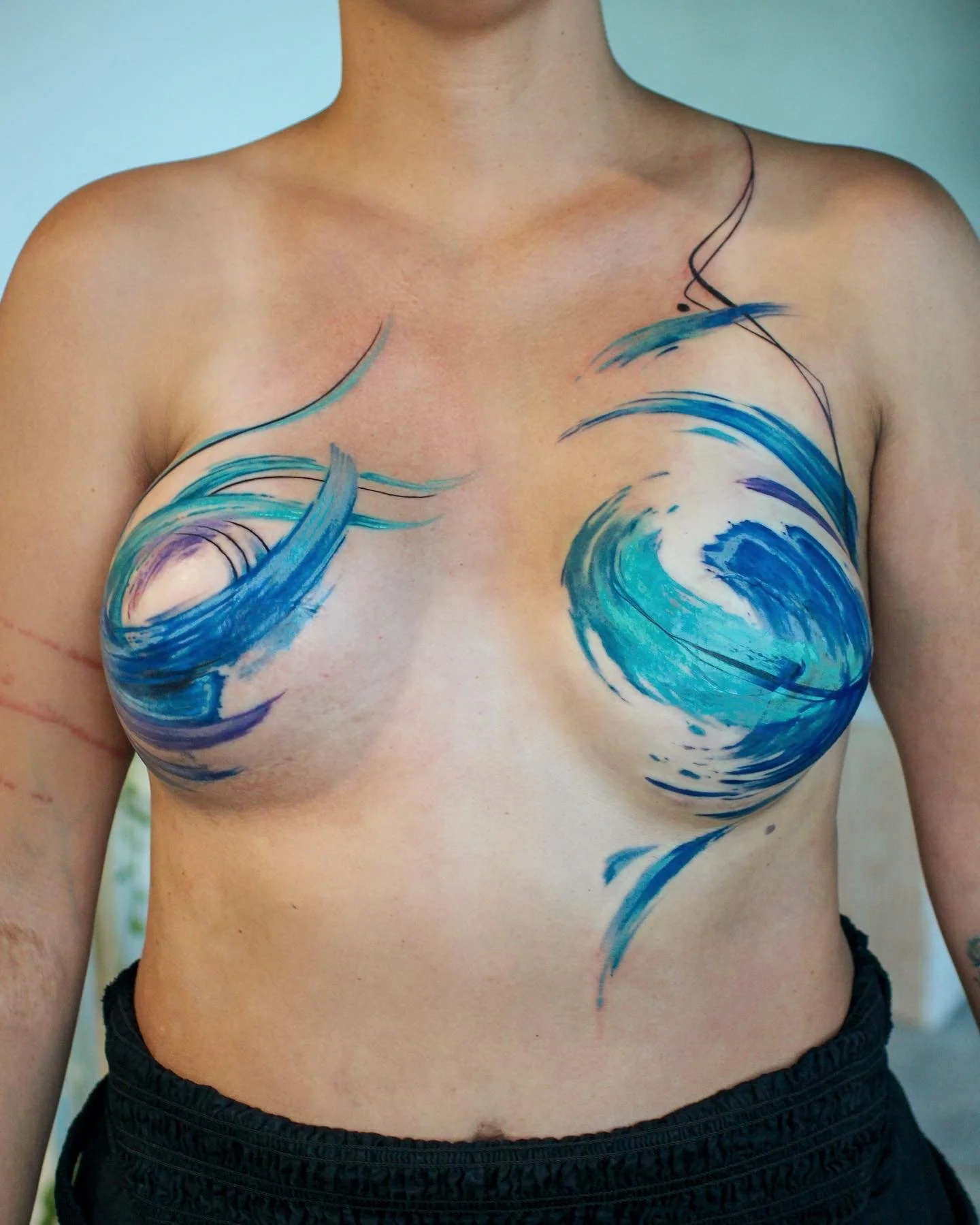A person with body paint of blue ocean waves on their chest and shoulder.
