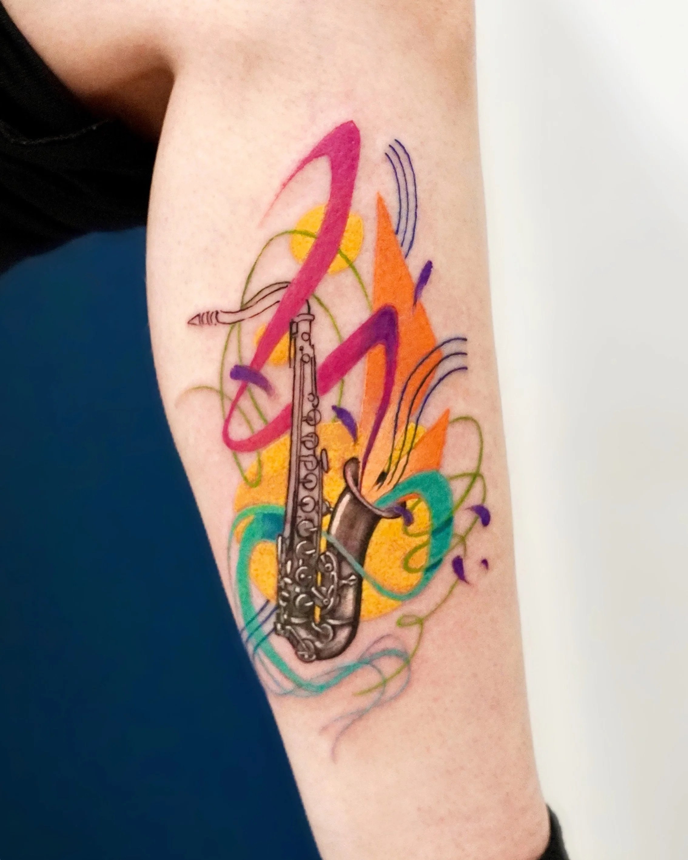 Colorful tattoo of a saxophone with abstract colorful shapes and lines.