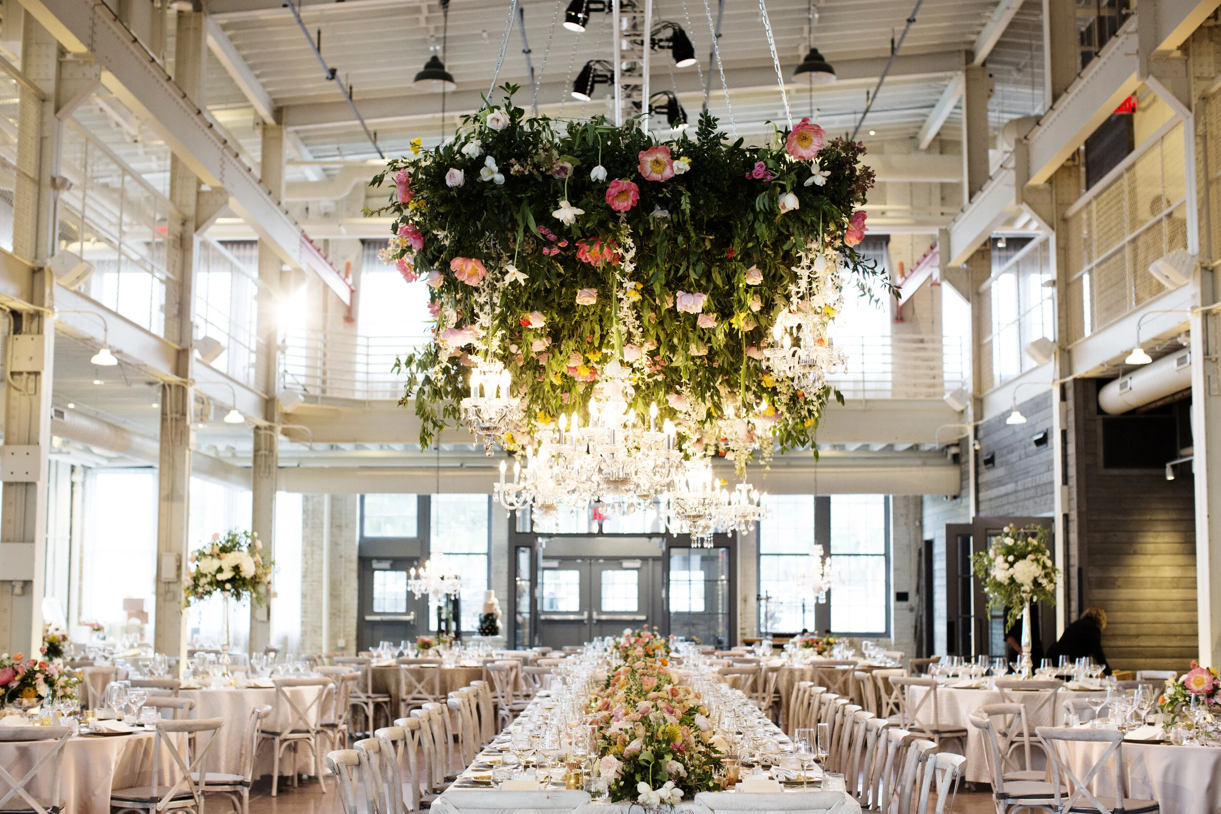 Elegant banquet hall with long dining tables, floral centerpieces, crystal chandeliers, and a large floral chandelier hanging from the ceiling.