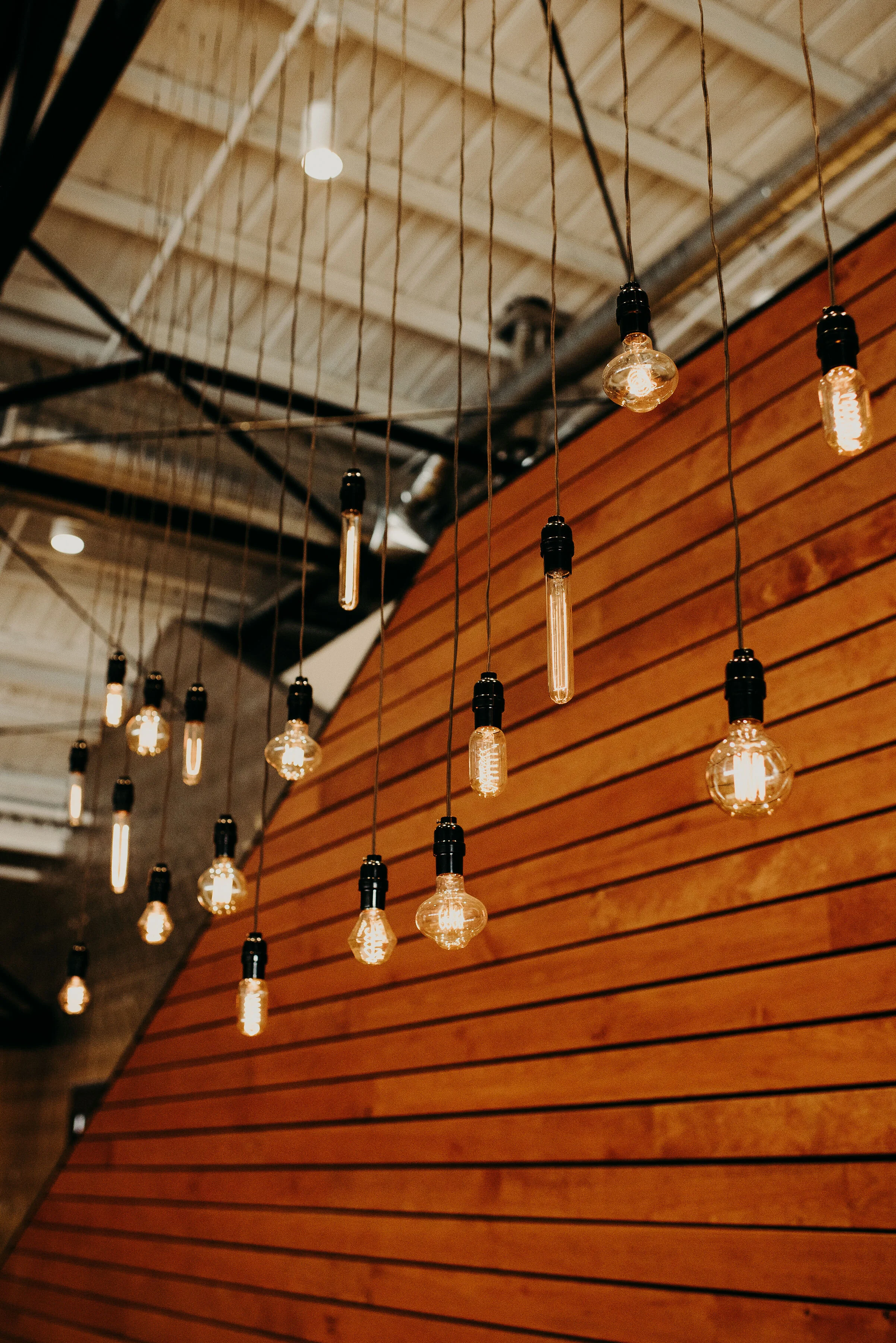 String of Edison-style light bulbs hanging from cords in a room with a slanted wood-paneled wall and an exposed ceiling.