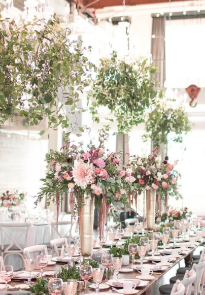Long banquet table decorated with pink and white flower arrangements and glassware in a bright, elegant setting.