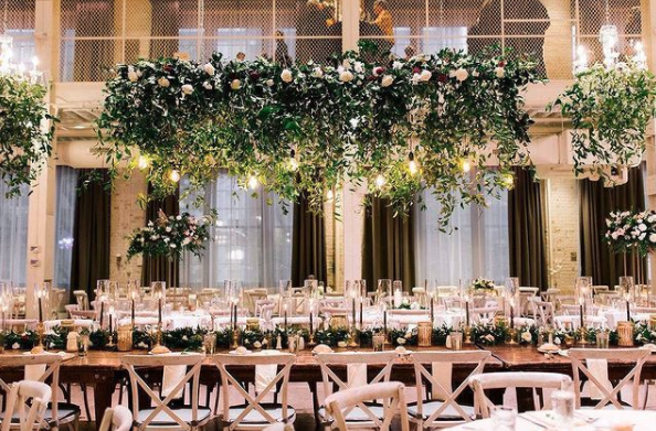 Elegant banquet table setup with floral centerpieces and hanging greenery in a decorated event hall.