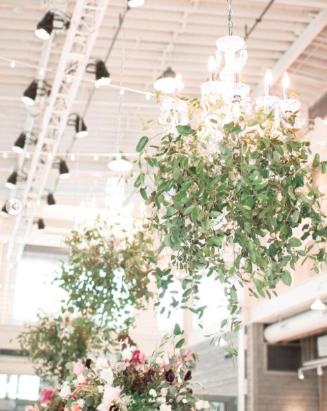 A chandelier decorated with green foliage hangs from a ceiling, with some flowers visible below.