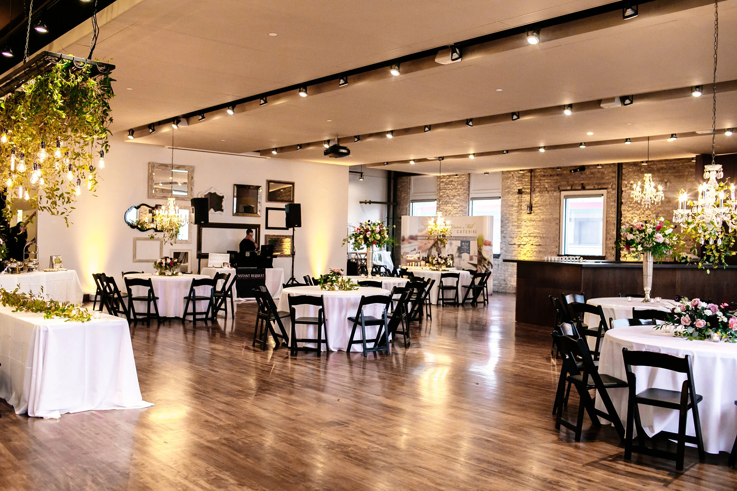 Elegant event space decorated with white tablecloths, floral centerpieces, and hanging chandeliers for a celebration or wedding reception.