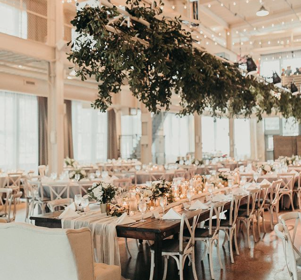 Decorated banquet hall with long tables, floral centerpieces, candles, and string lights hanging from the ceiling, ready for a celebration.