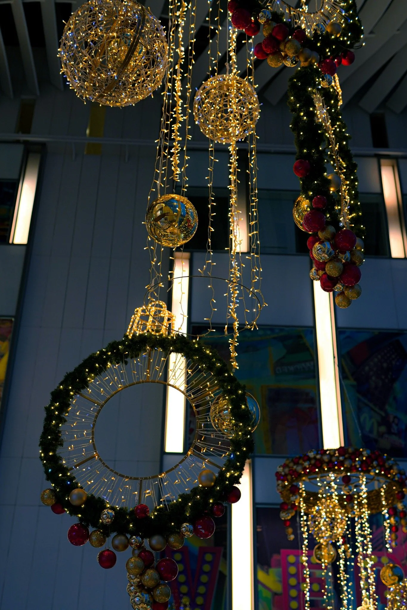 Large illuminated wreaths, glowing spheres and red and gold ornaments suspended in a commercial interior.