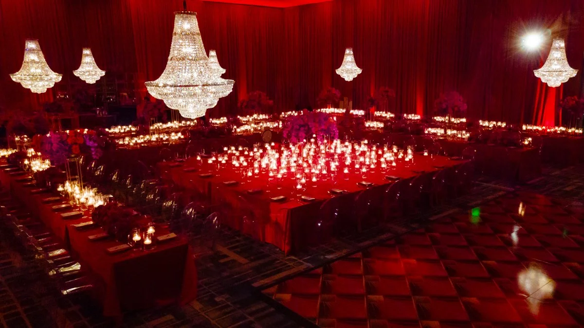 Moody luxury event design with crystal chandeliers, candlelit tables, and dramatic red uplighting in an elegant ballroom.