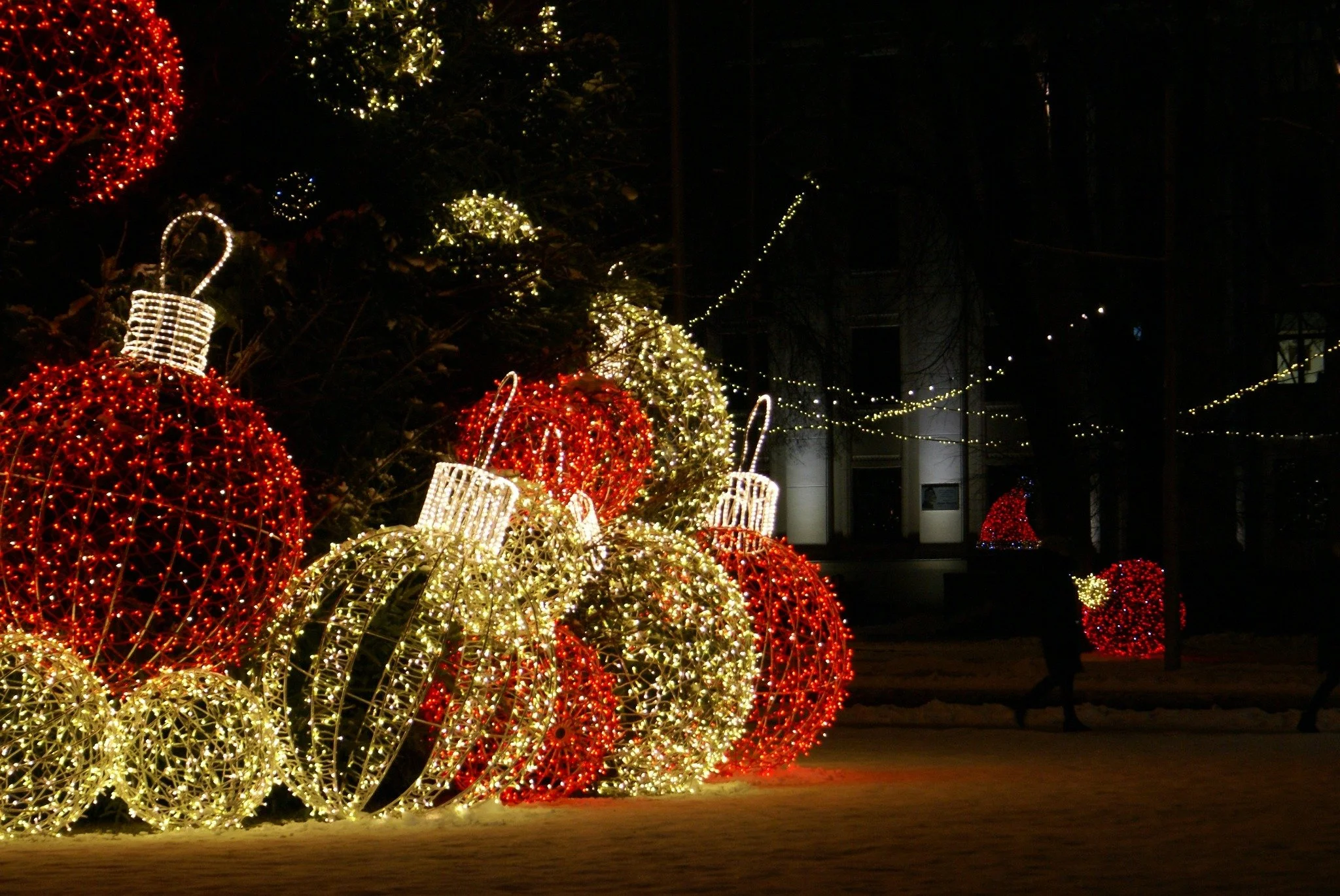 Oversized red and warm white illuminated Christmas ornaments displayed outdoors at night.