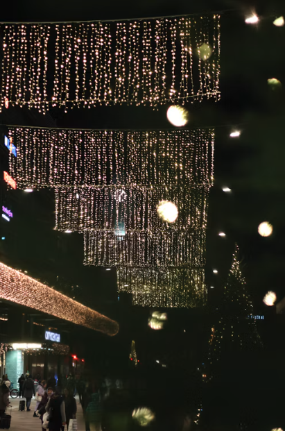 Large rectangular curtains of warm white holiday lights suspended above an outdoor commercial walkway.