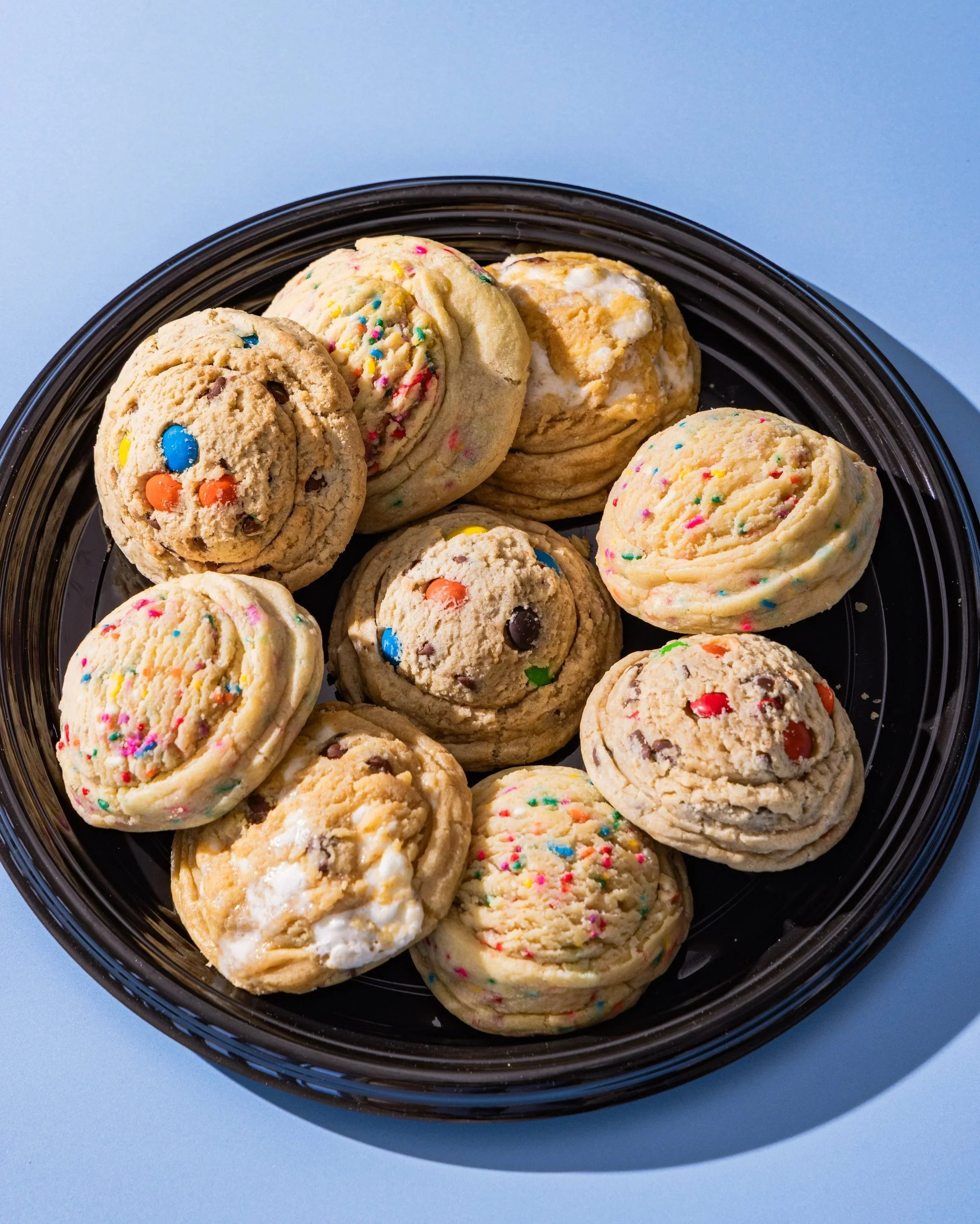 Plate of assorted cookies with colorful sprinkles, chocolate chips, and white icing, on a light blue background.