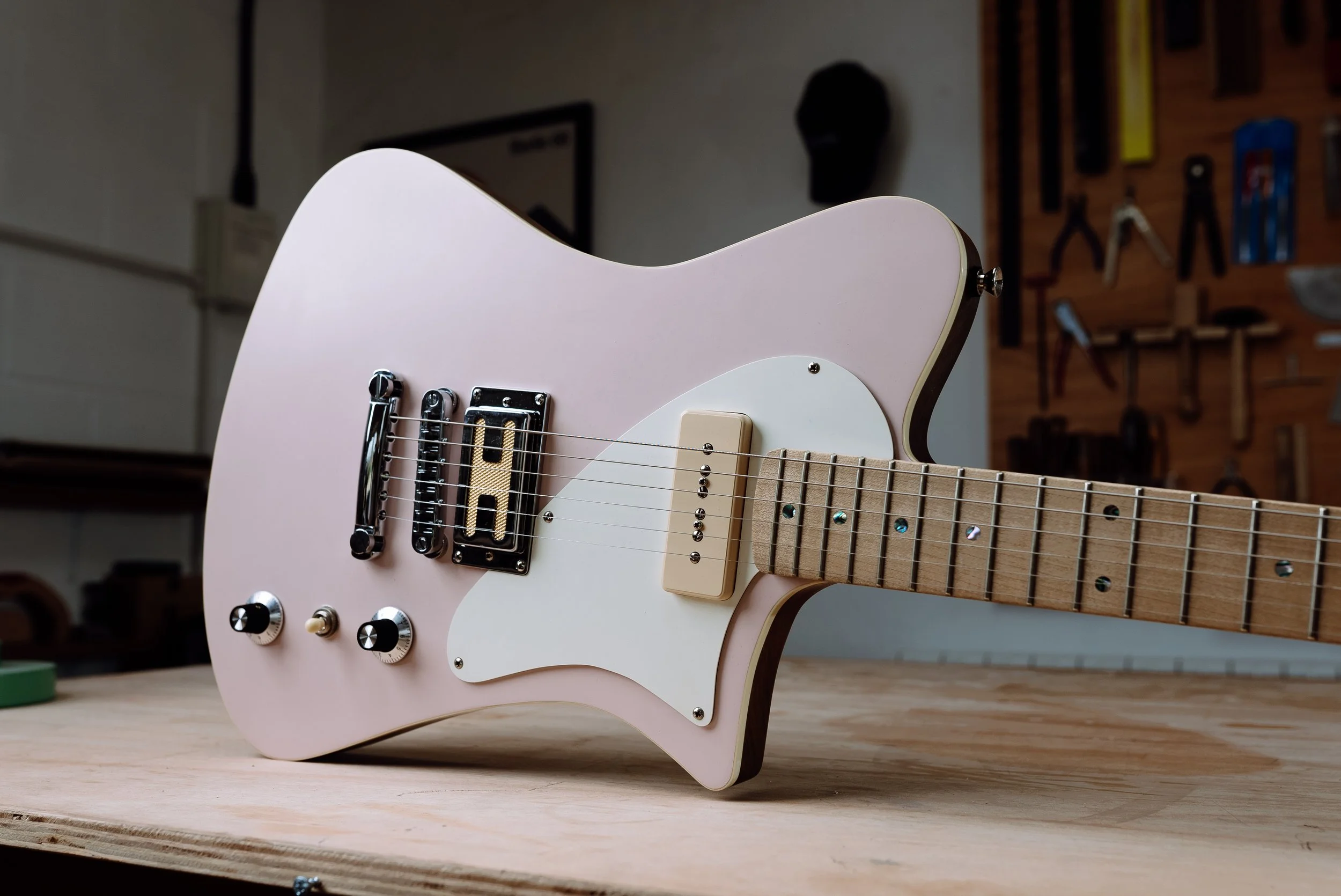 Pink electric guitar on a wooden table in a workshop setting.