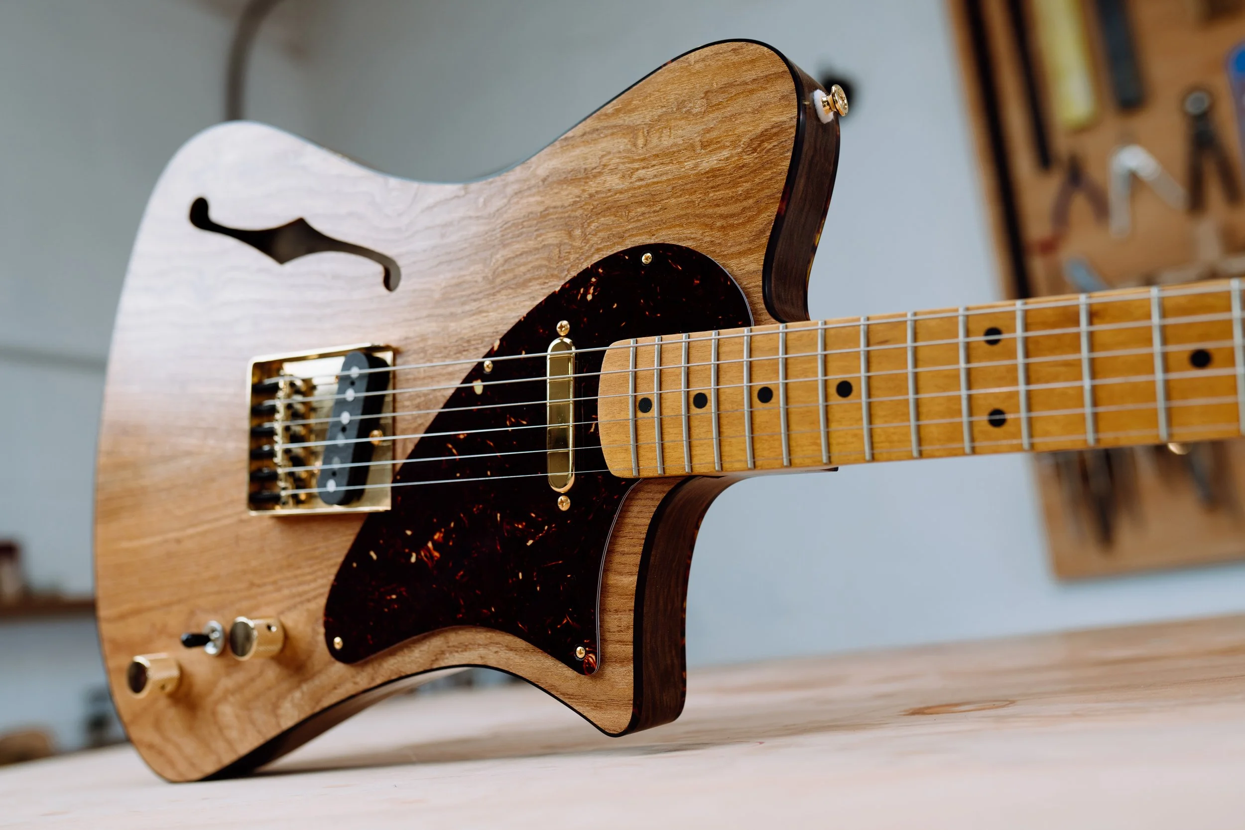 Close-up of a wooden electric guitar with a semi-hollow body, gold hardware, and maple fretboard.