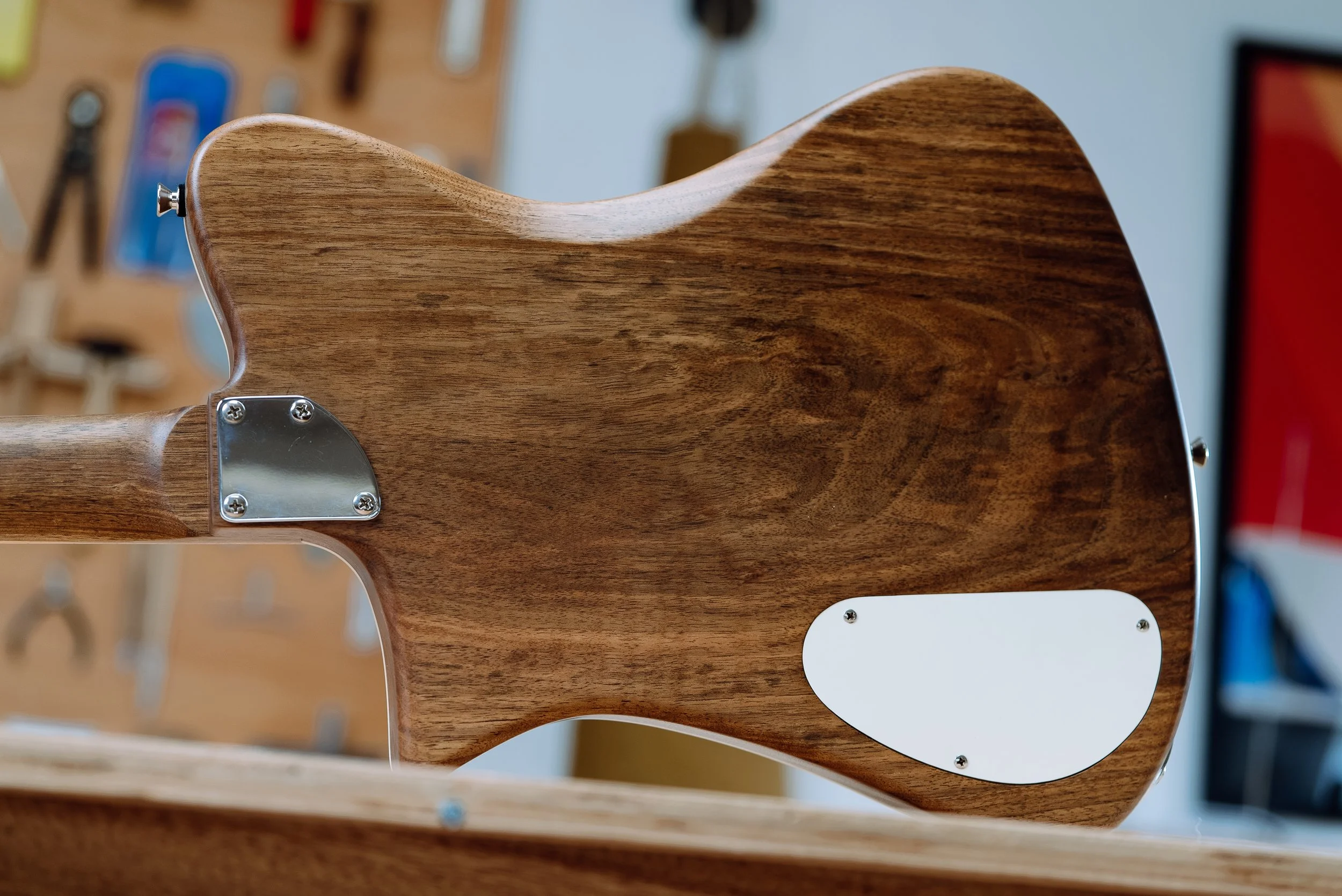 Back of a wooden electric guitar body with a metallic plate and white backplate, in a workshop setting.