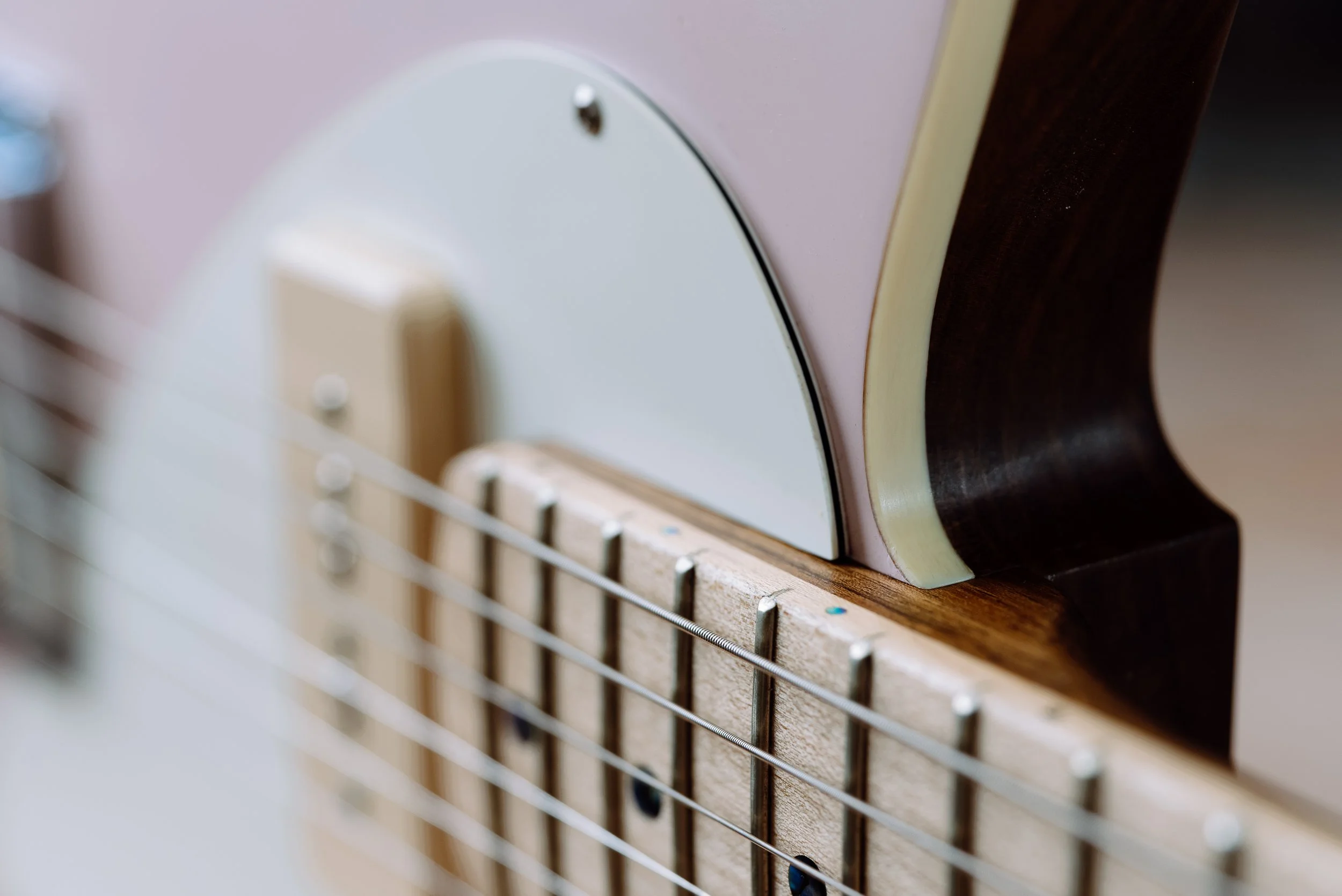 Close-up of guitar strings and fretboard with a focus on the body edge and pickguard.
