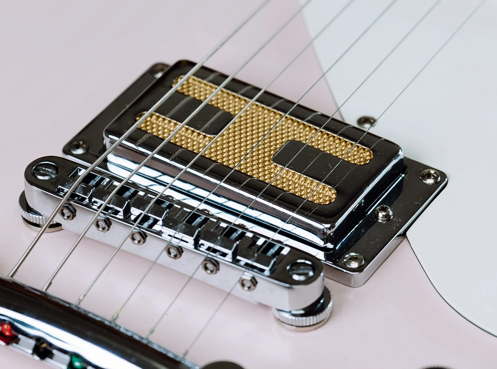 Close-up of an electric guitar bridge and pickup with gold and chrome finish, featuring strings and a modern design.