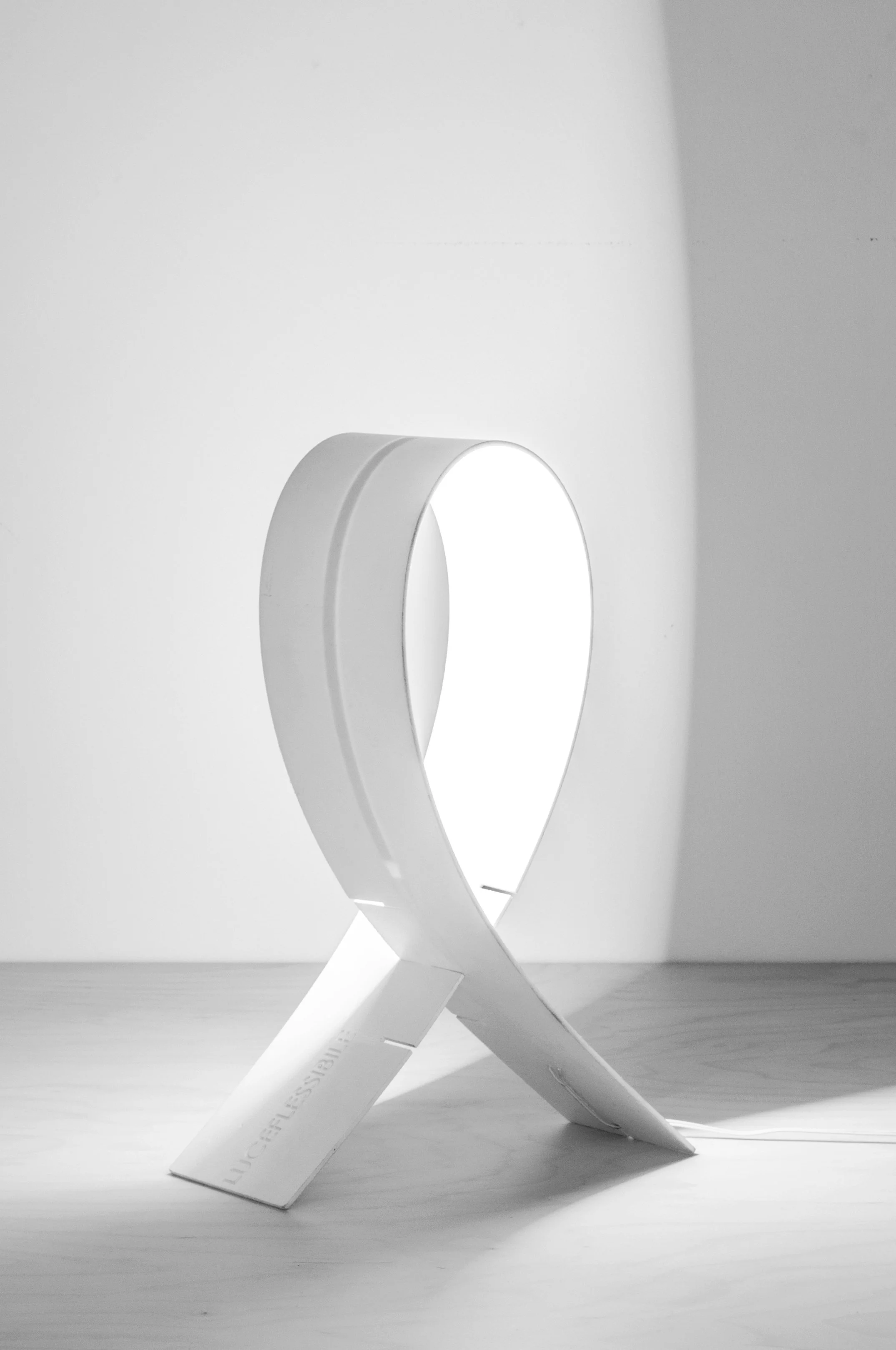 A modern, minimalist table lamp with a sleek, white, looped design on a wooden surface, casting soft shadows.
