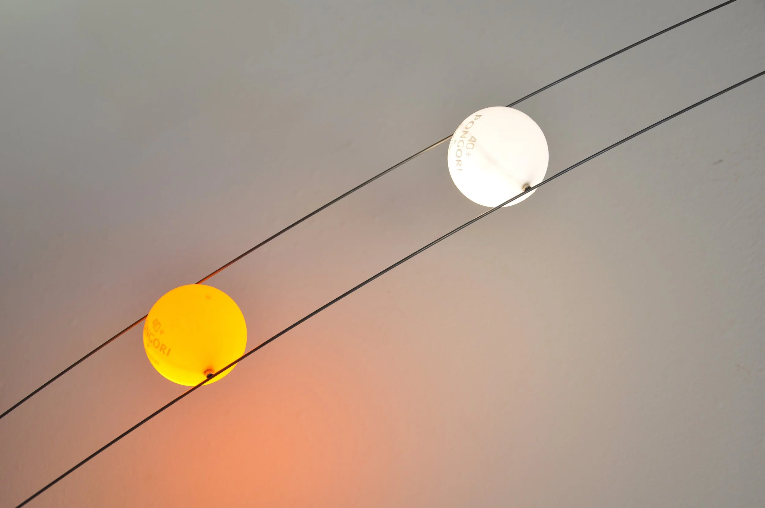 Two spherical lamps, one yellow and one white, hanging from wires on a plain ceiling.