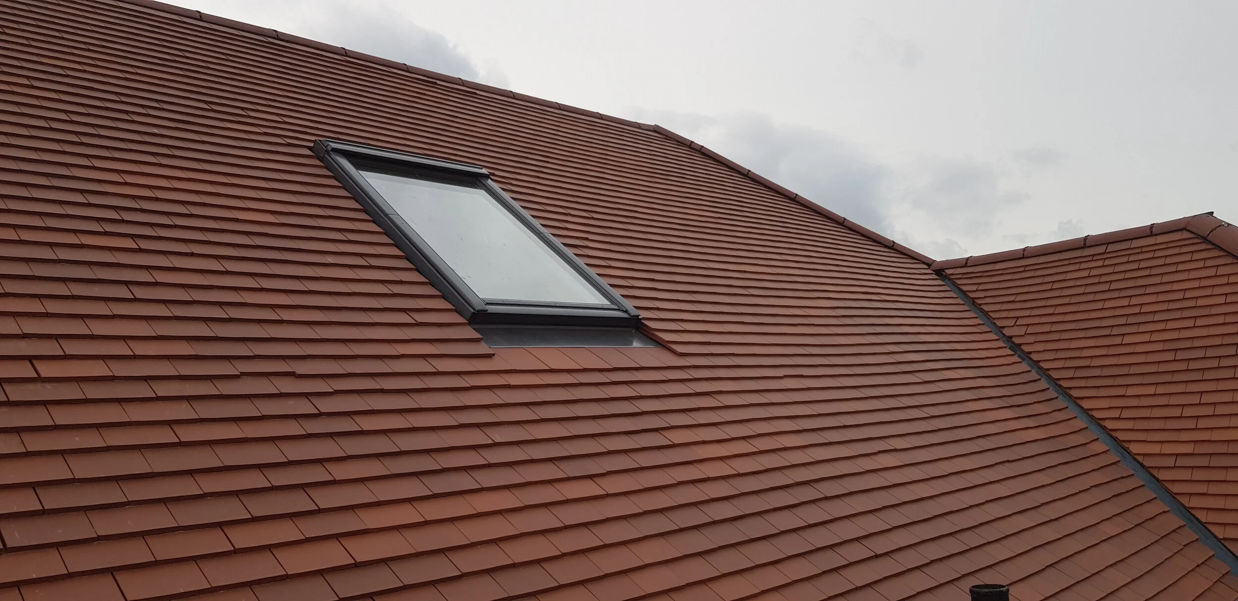 A roof with red clay tiles and a large rectangular skylight window.