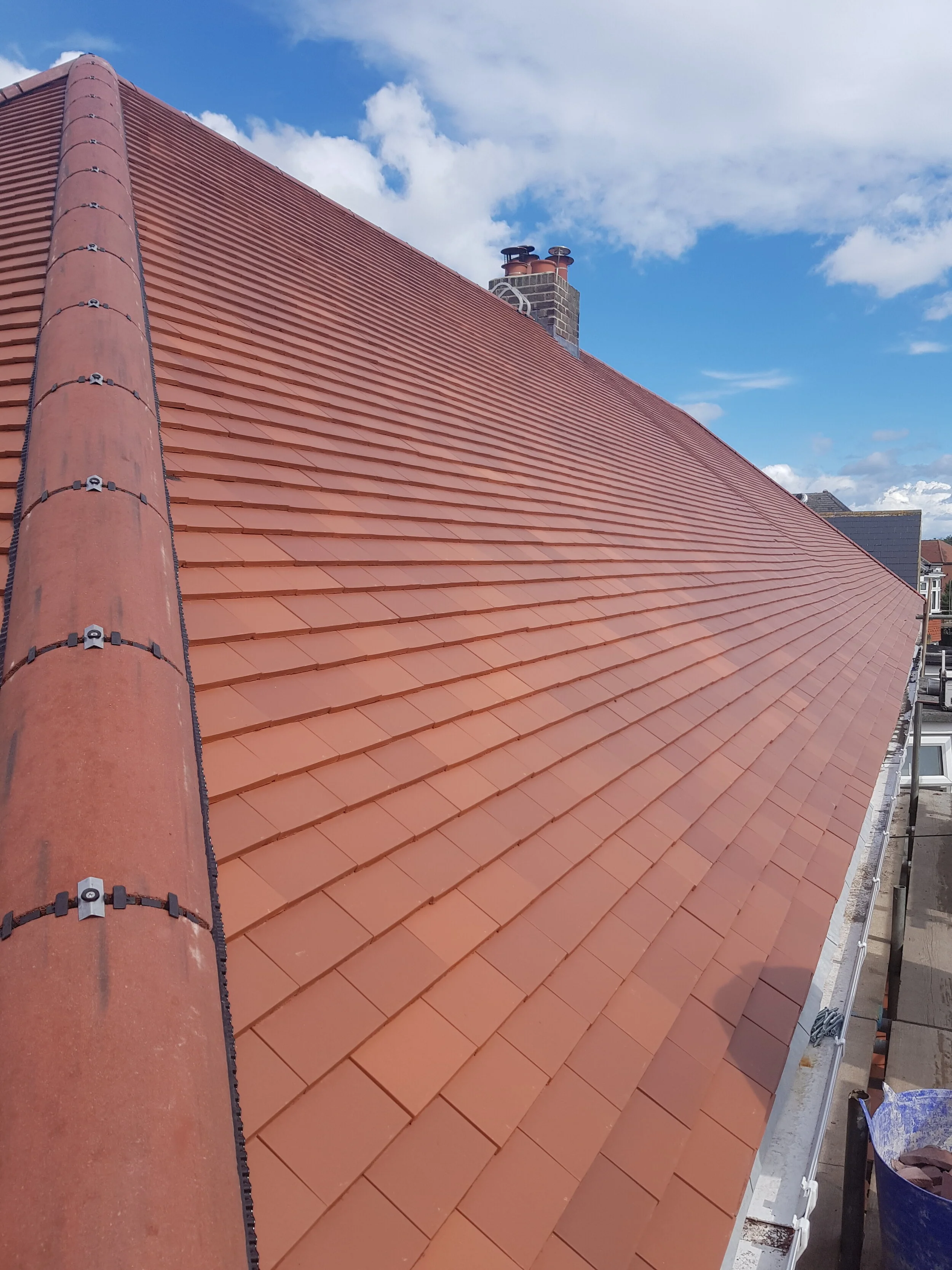 Red tiled roof with a chimney and a blue sky with clouds.