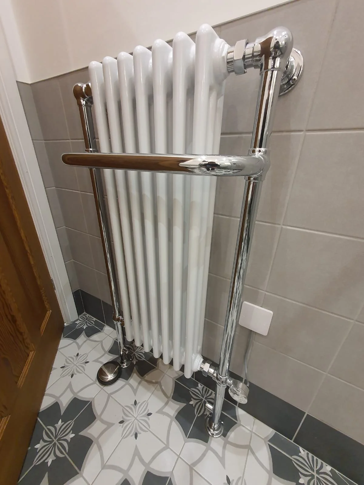 A white cast iron radiator with a chrome frame in a tiled bathroom.