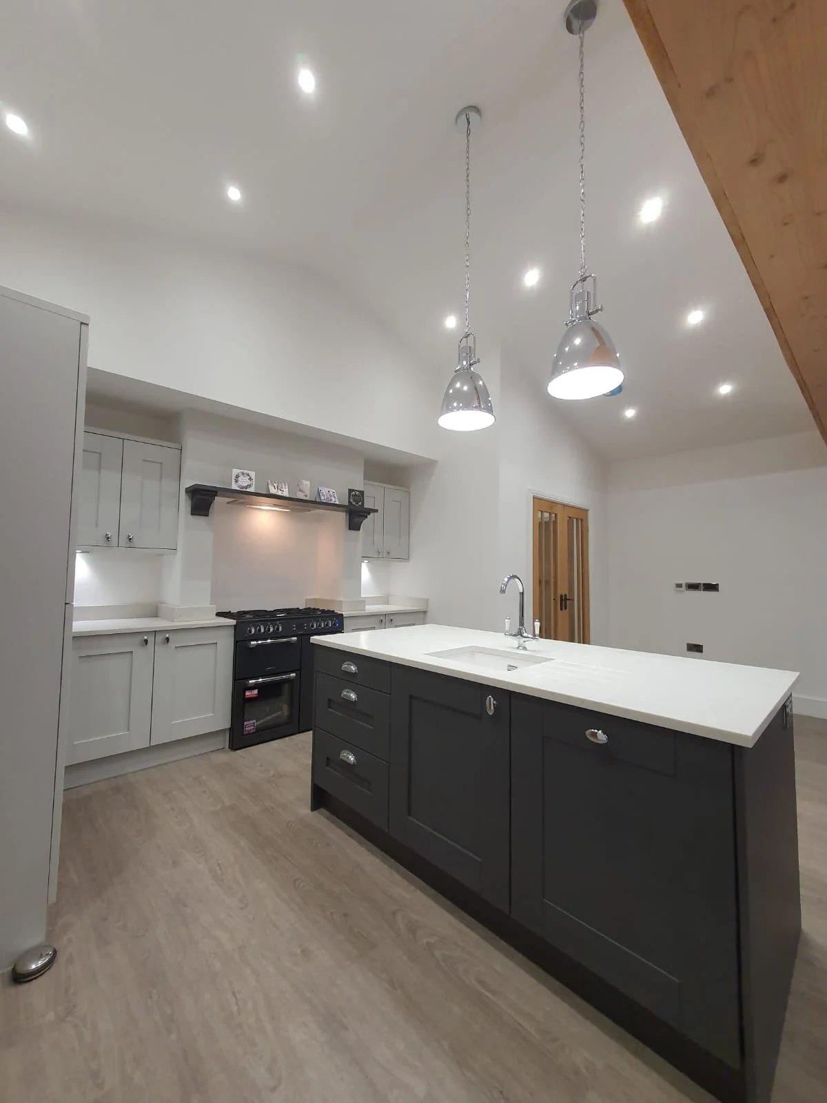 Modern kitchen with light grey cabinets, a black stove, a black kitchen island with a white countertop, pendant lights, and light wood flooring.