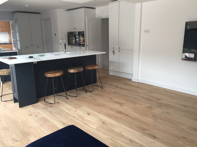 Modern kitchen with a white island, four wooden stools, white cabinetry, and wood flooring.