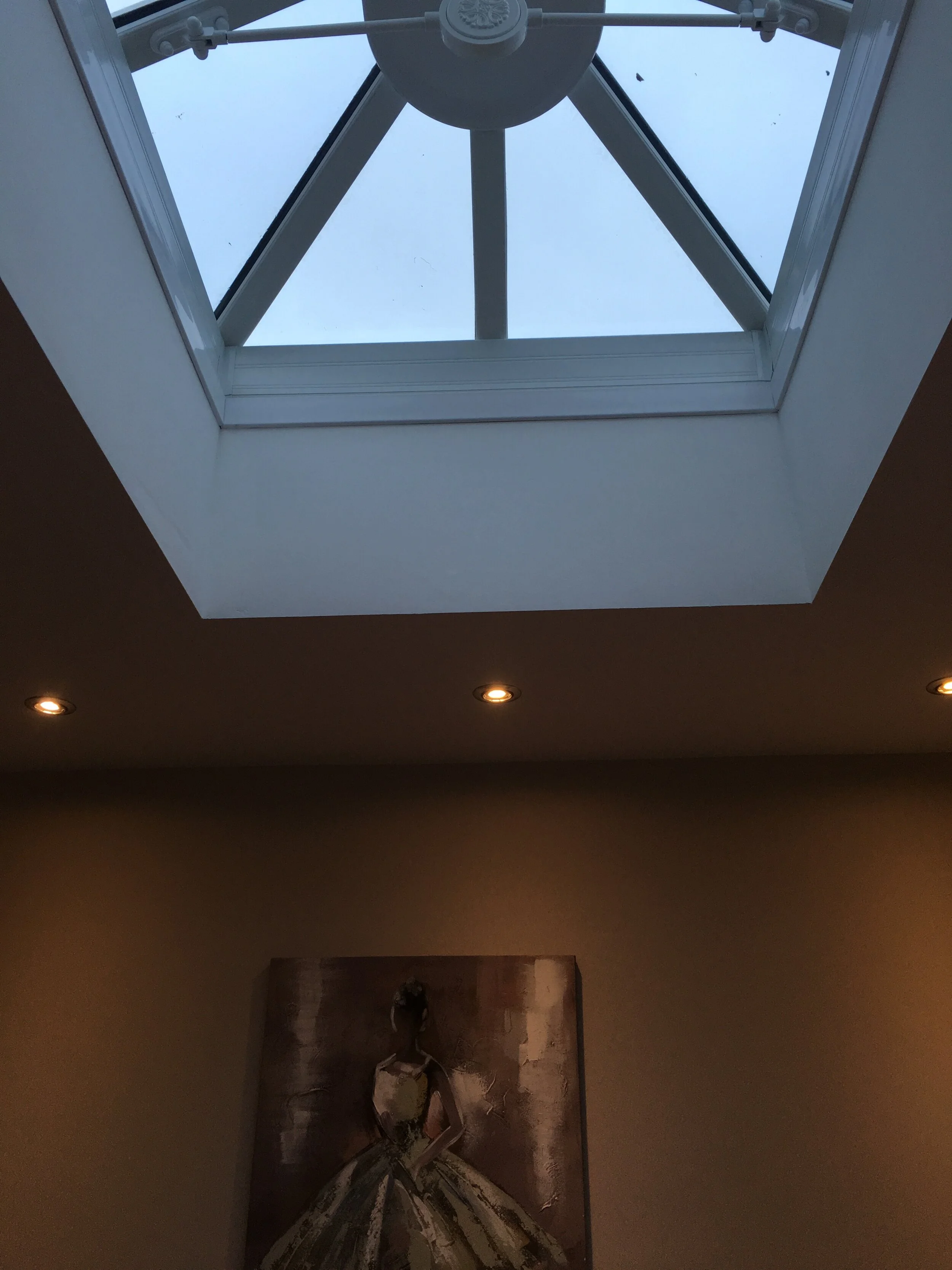 View of a square skylight with a fan and support beam, ceiling with recessed lighting, and a painting of a woman in a gown on a wall.