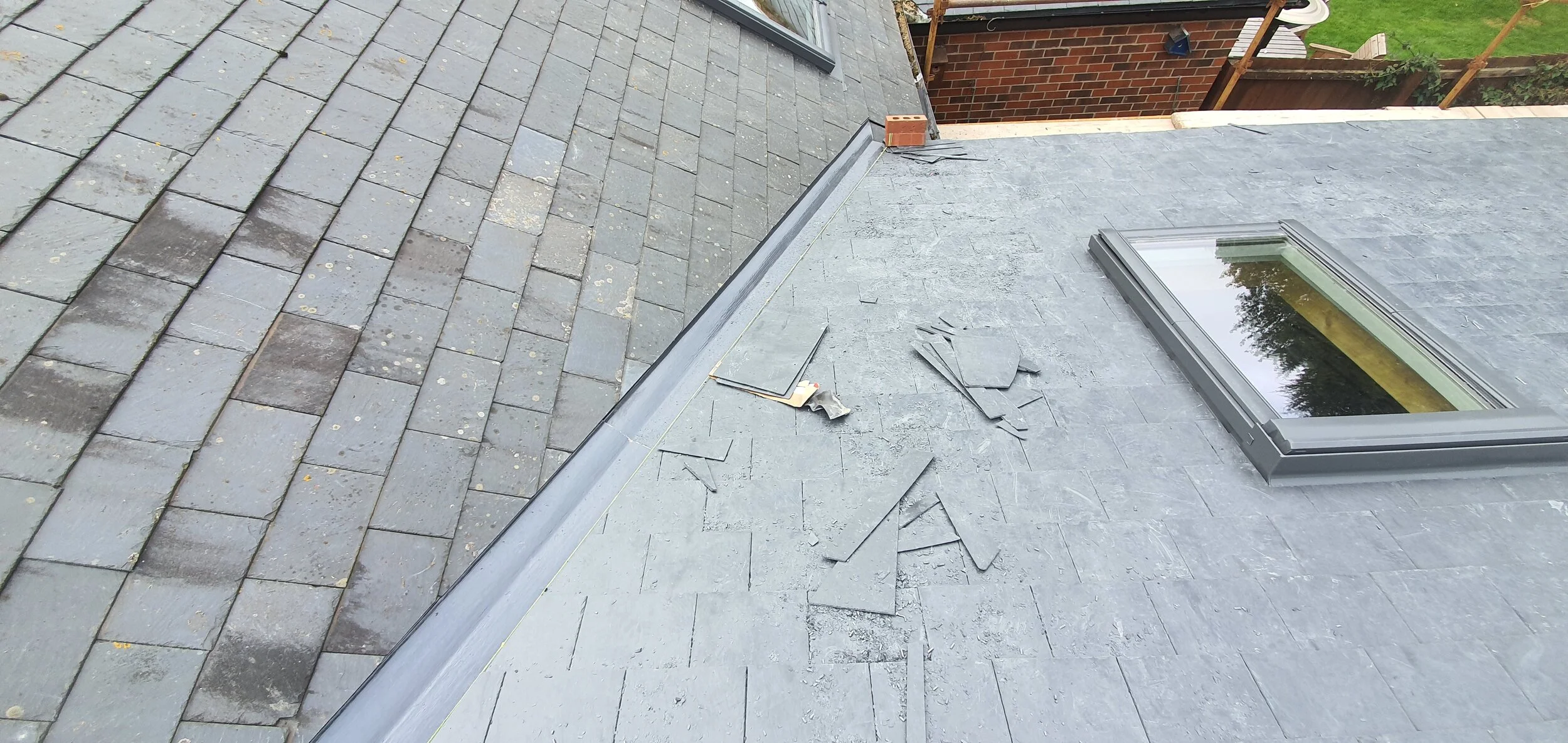 Parts of the roof are being worked on, with some loose roofing tiles and tiles of slate material scattered on the black slate part of the roof; a skylight window is also visible.