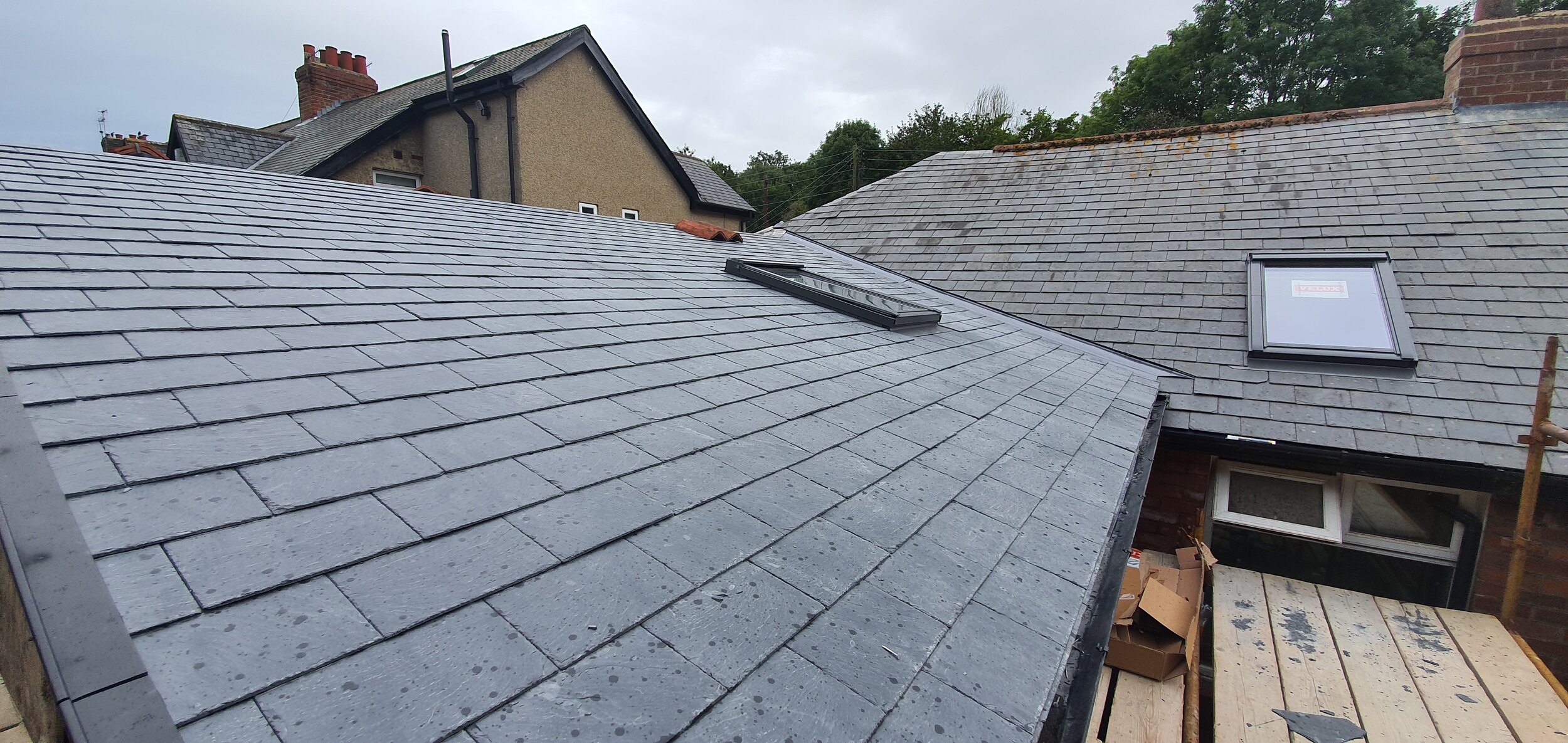 A residential roof with newly installed gray slate tiles, two skylights, and a small section of scaffolding and construction materials.