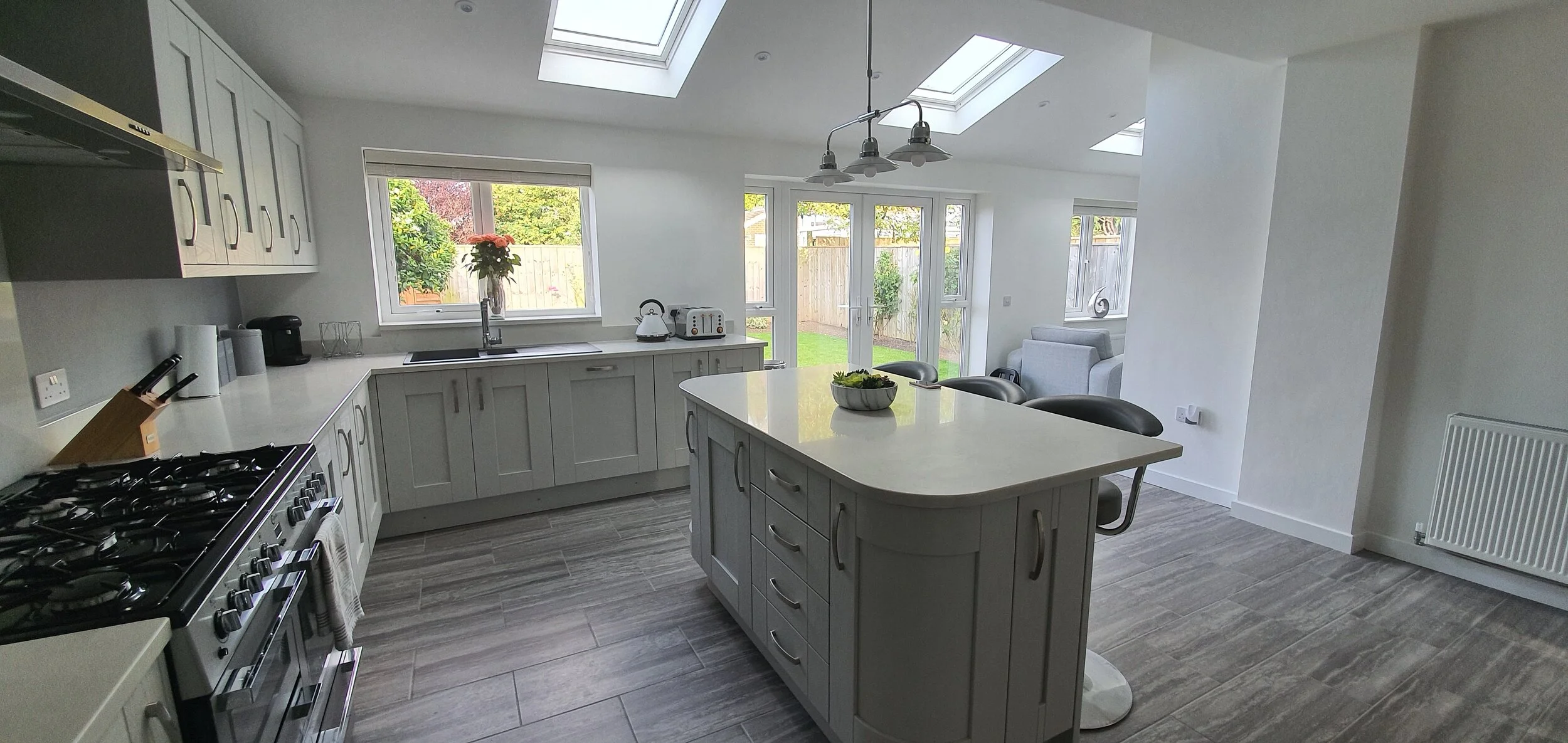 Modern kitchen with white cabinets and an island, stainless steel stove, and large windows and skylights to let in natural light. There's a bowl of greens on the island.