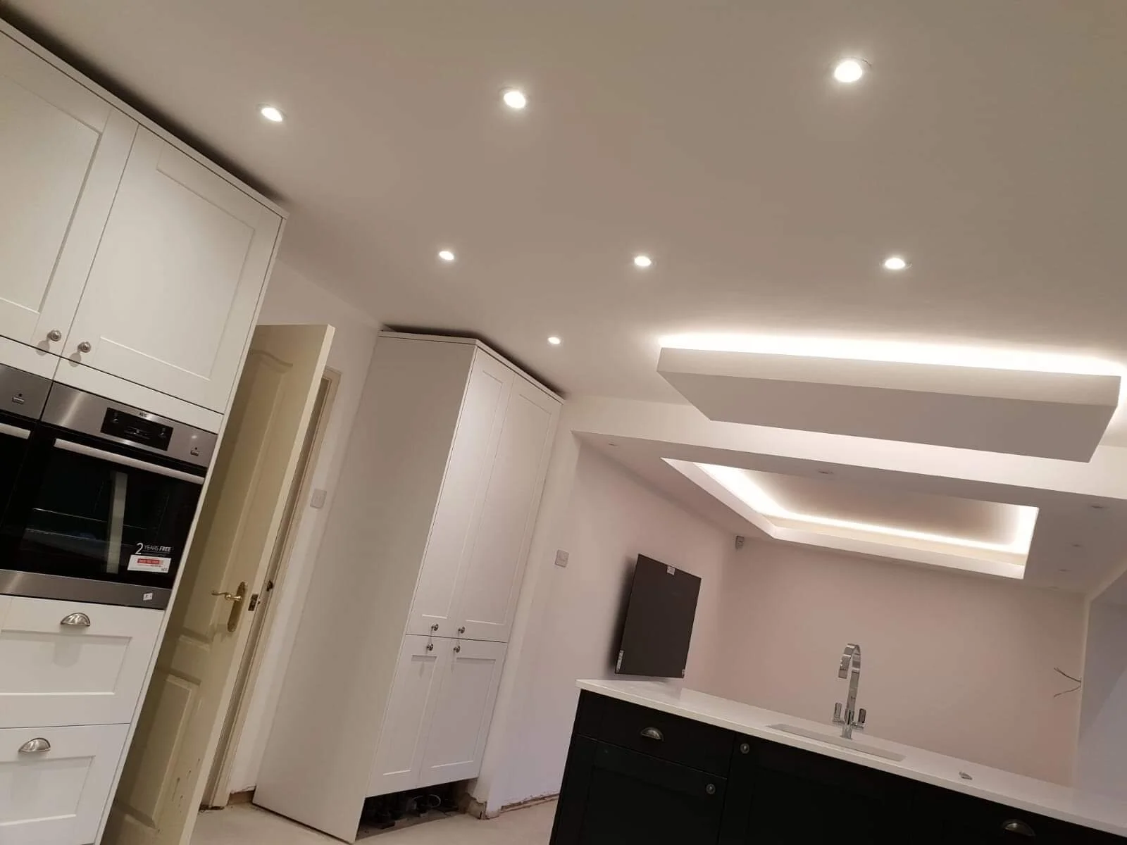 Modern kitchen with white cabinets, black island, built-in oven, and ceiling with recessed lighting and LED strip lighting.