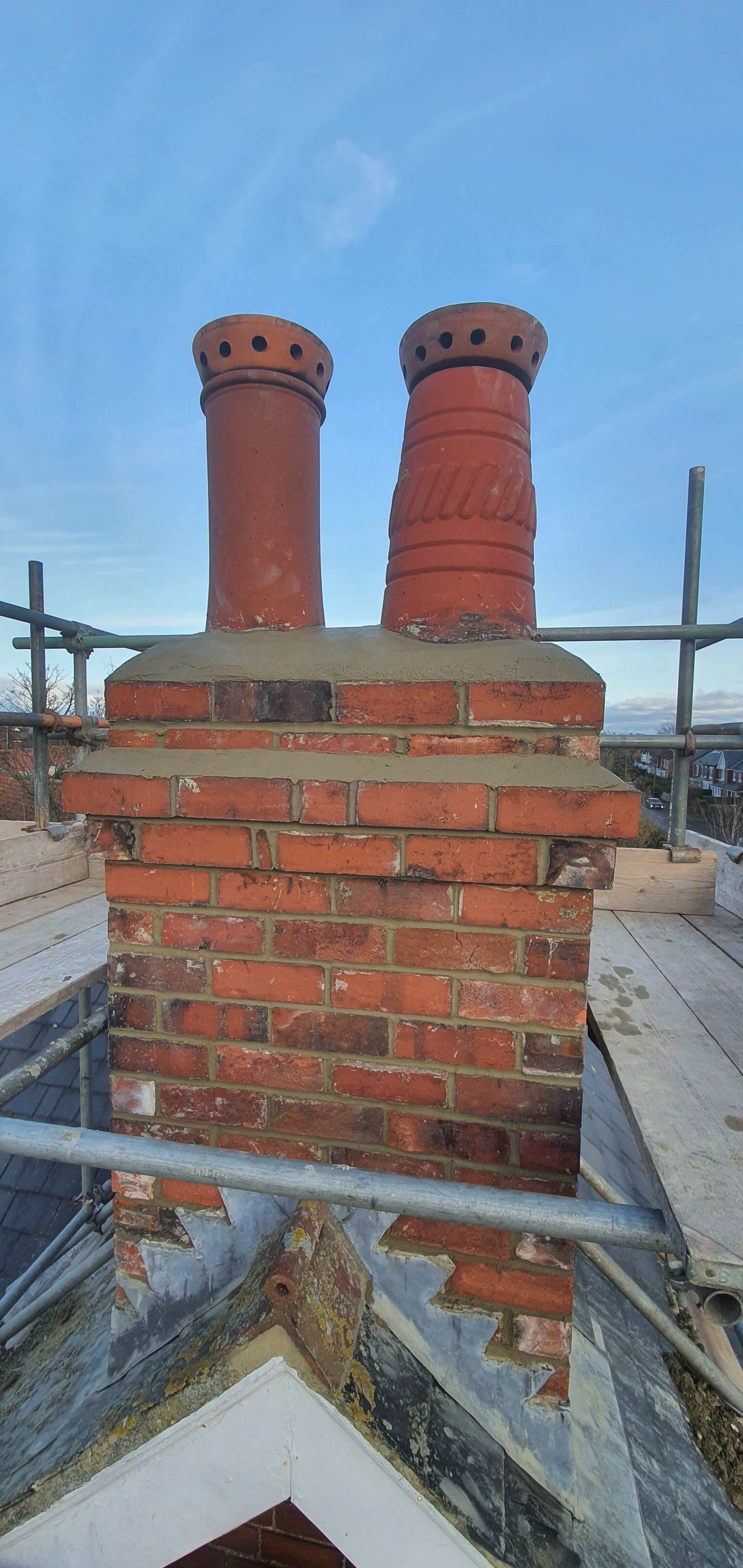 Close-up of a brick chimney with two terracotta chimney pots under a blue sky on a building under construction or renovation.