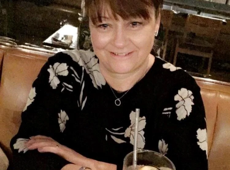 A woman with short hair sitting at a restaurant table with a drink and straw, smiling at the camera.