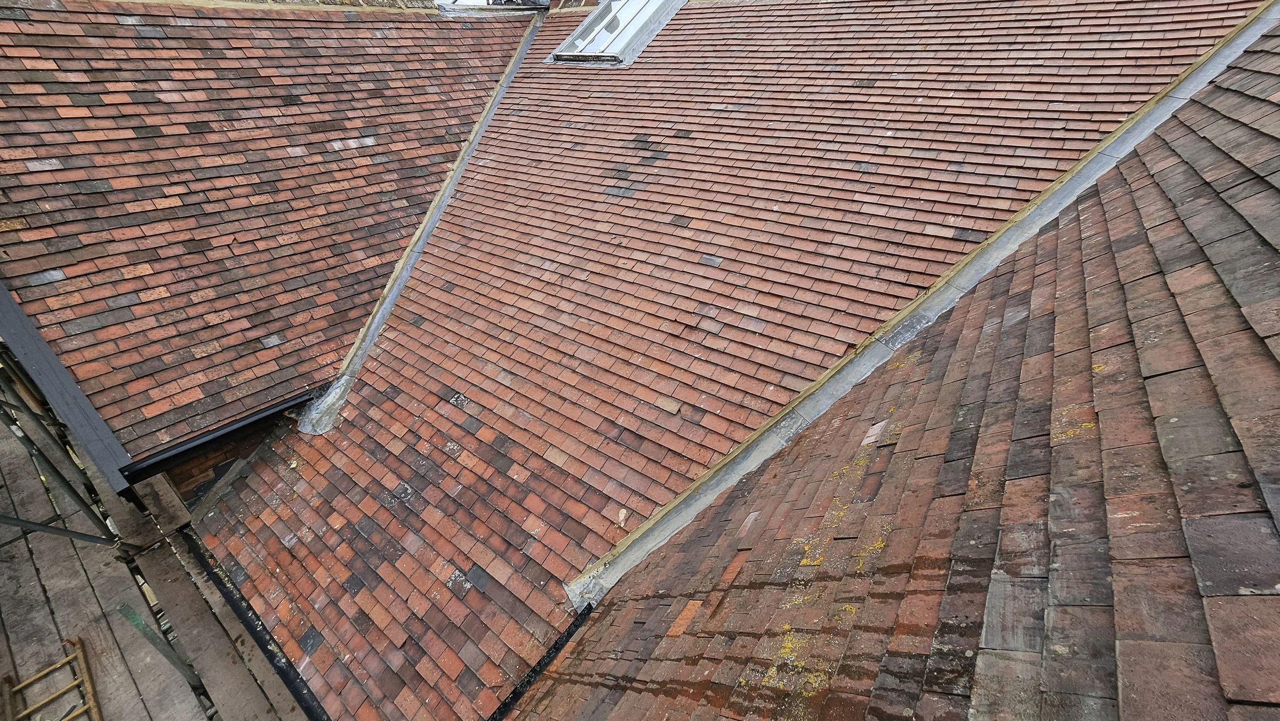 Multiple sections of a sloped roof with reddish-brown shingles, showing signs of weathering and moss growth, with a skylight window visible.