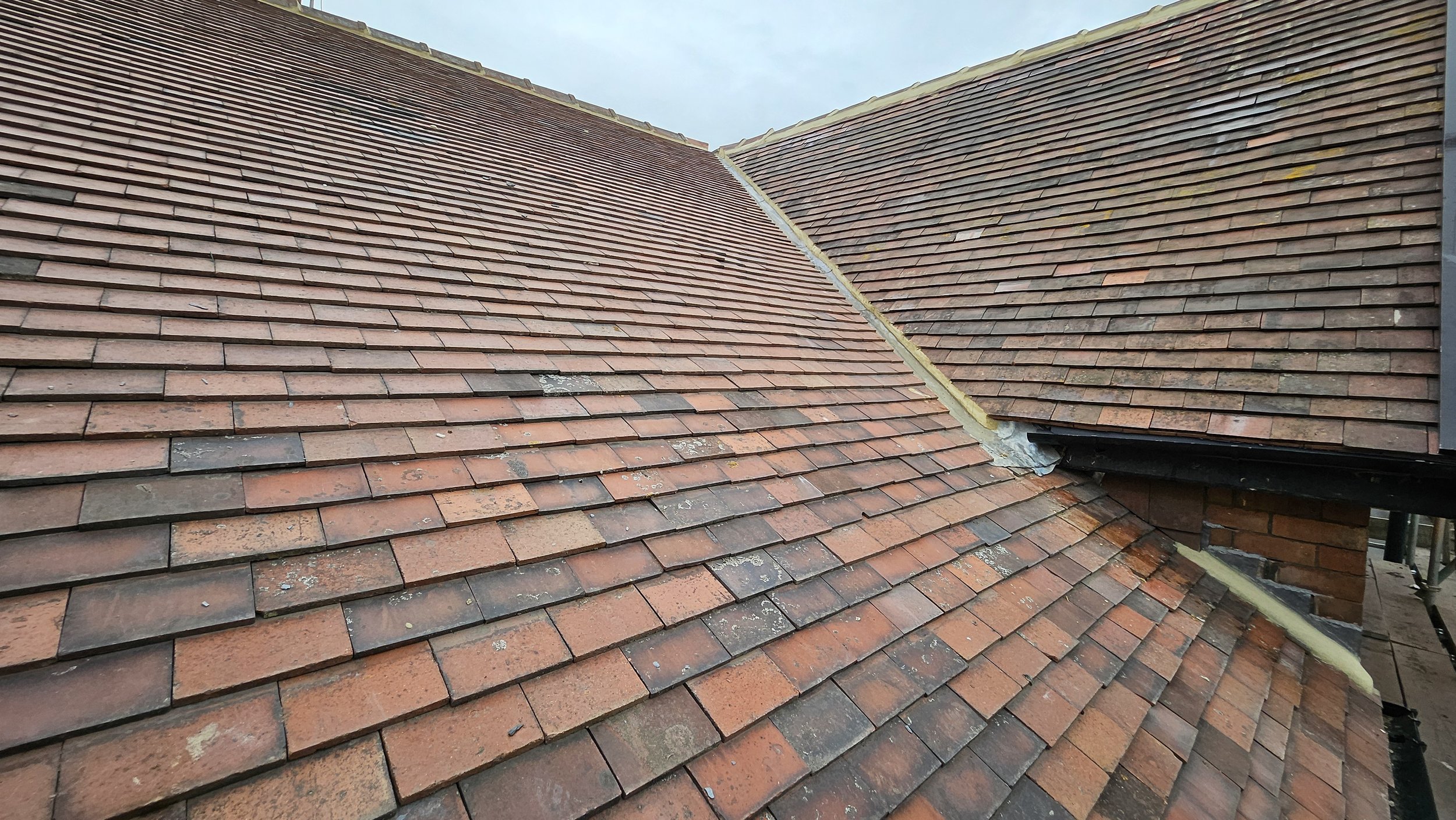 Close-up view of a tiled roof with red clay tiles, showing some signs of weathering and moss growth, with a section under construction or repair.