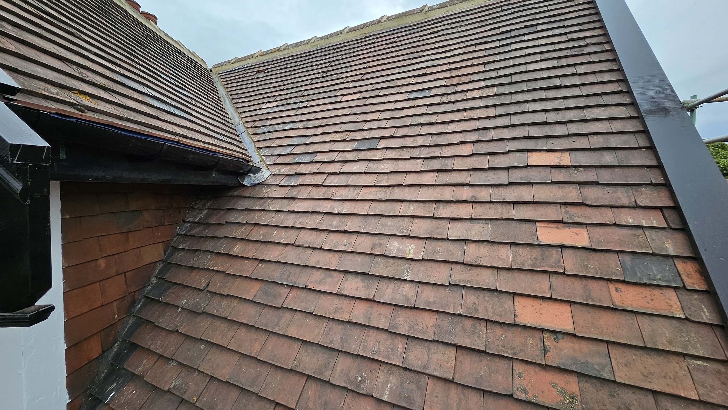 Close-up view of a tiled roof with overlapping reddish-brown shingles, showing different angles and textures.