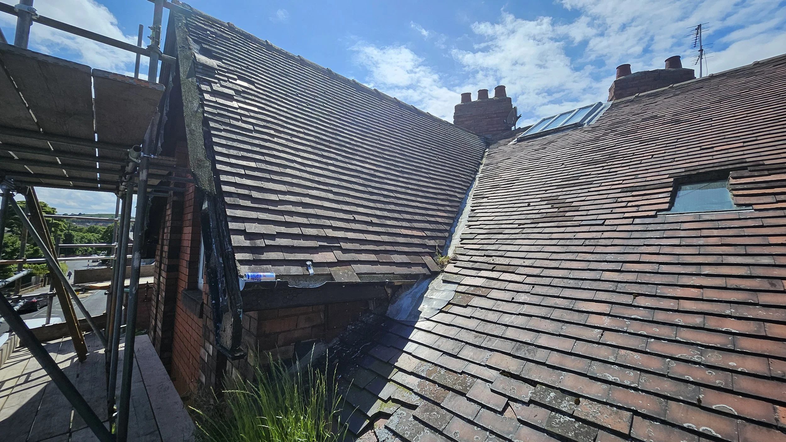 Roof of a building with visible signs of wear and repair scaffolding on the left side, under a partly cloudy sky.