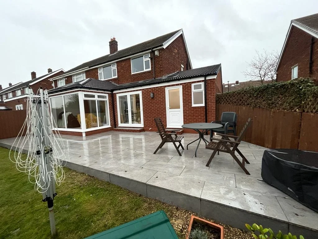 Backyard patio with outdoor furniture, including a table and chairs, and a brick house with a sliding door and windows.