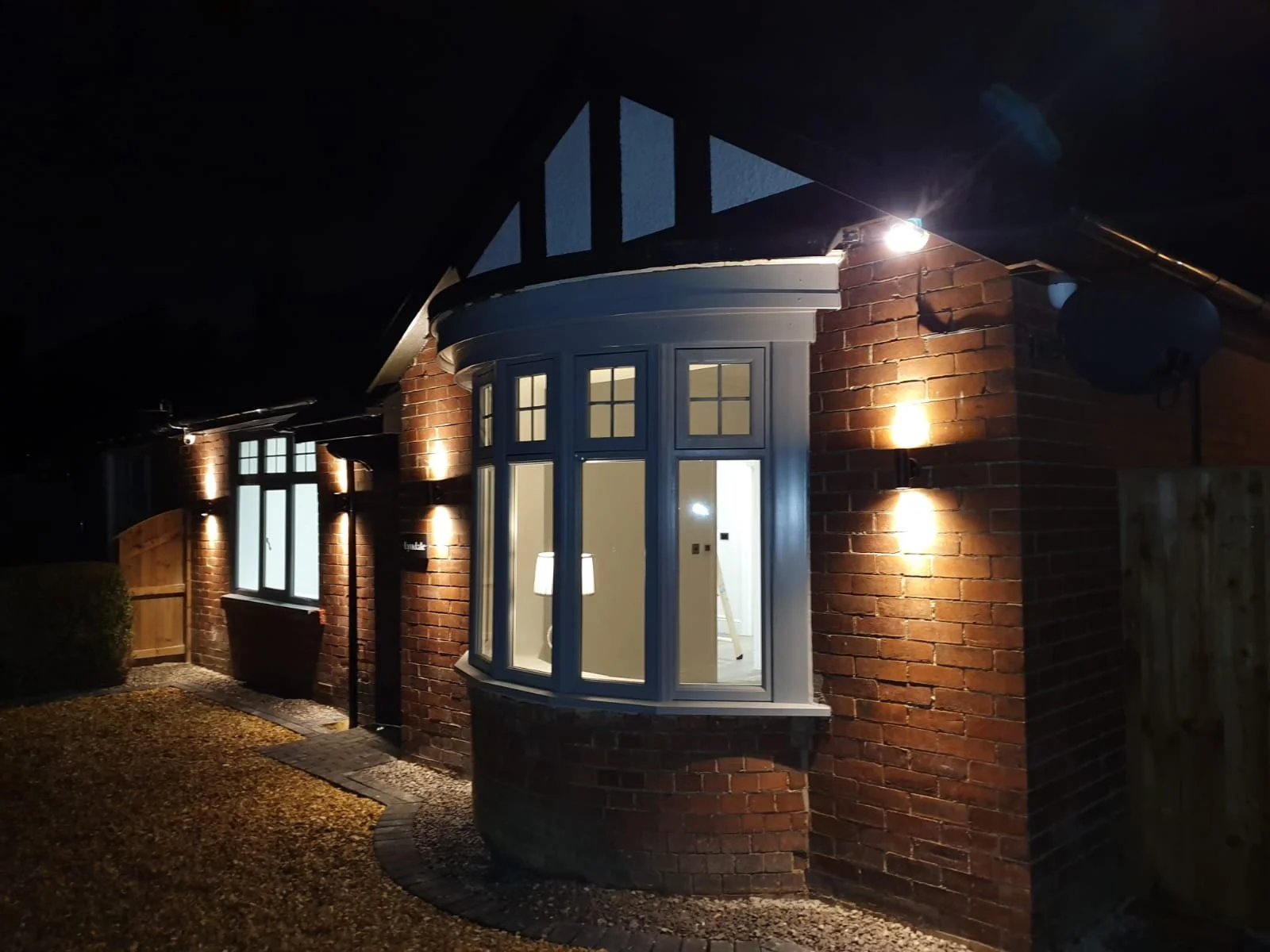 Brick house with illuminated exterior lights at night, bay window, and a lantern-style wall sconce.
