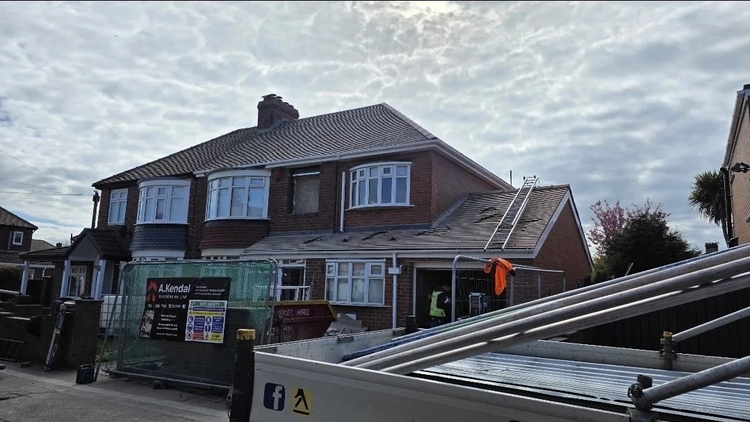 Construction workers working on the roof of a brick house with scaffolding and ladders, with cloudy sky overhead.