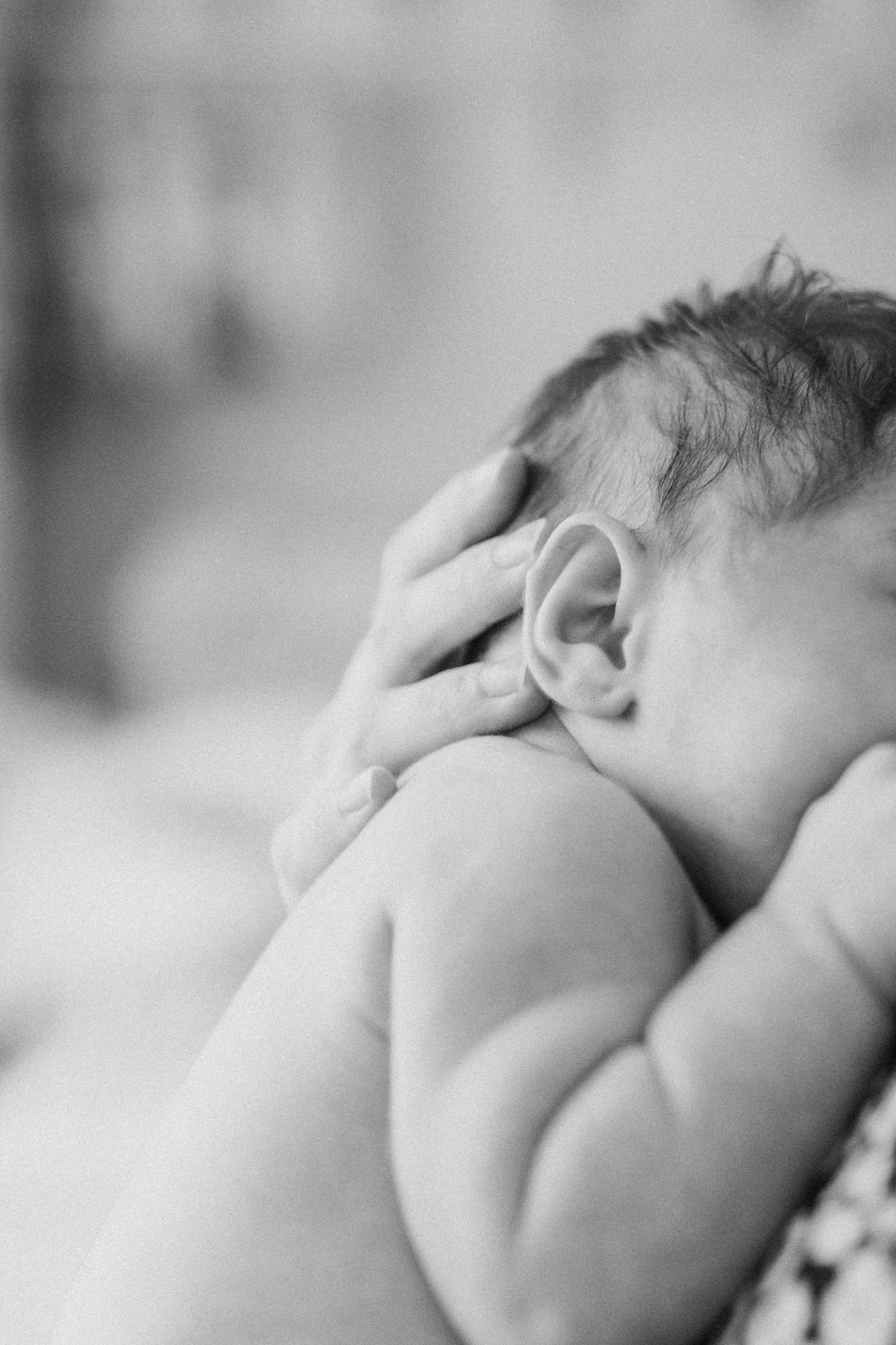A close up black and white photo of a mother cradling her baby's head.