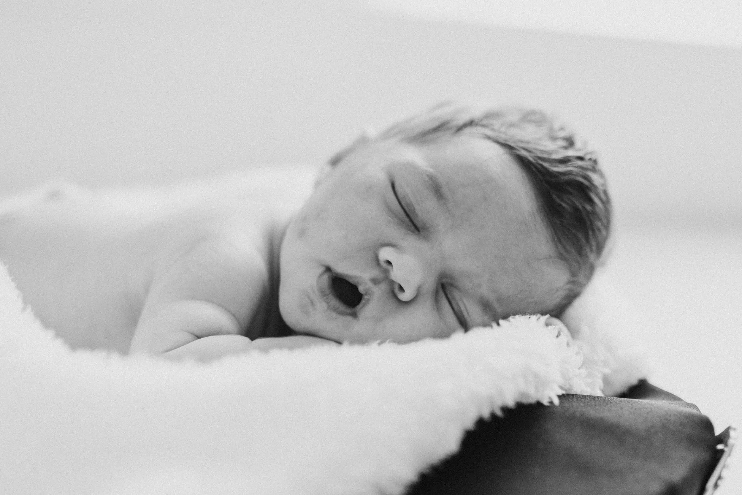 A soft, black and white photo of a sleeping newborn baby lying on a soft blanket, with a peaceful expression.