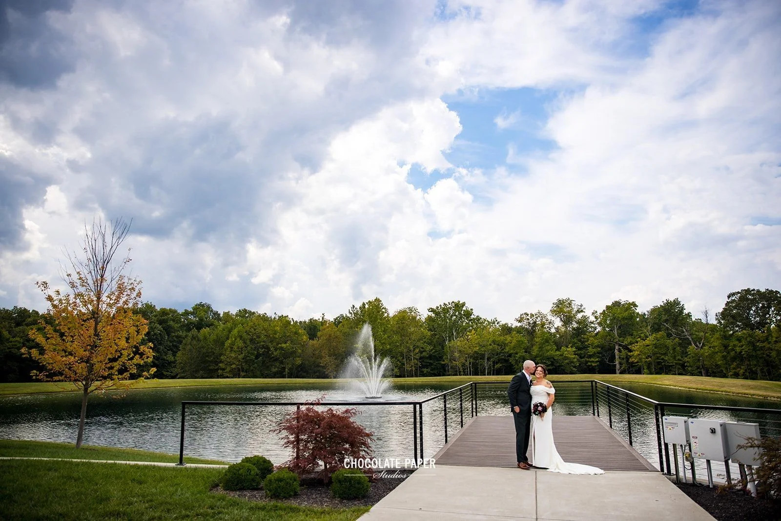 our beautiful bride and groom pose for wedding day photos on our pier with pond, fountain and forest backdrop near Cincinnati!